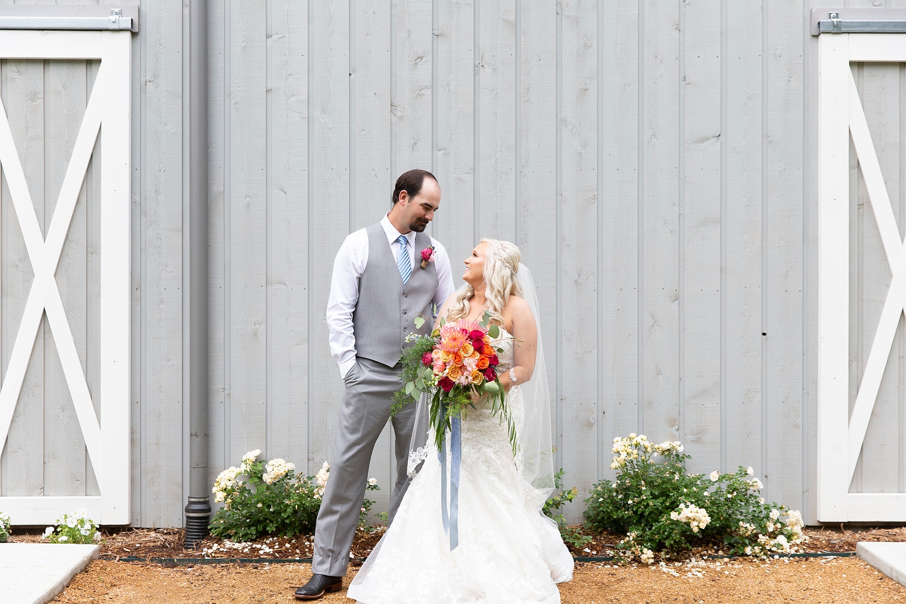 bride and groom pose by grey wooden barn in Dallas TX photographed by Randi Michelle Weddings