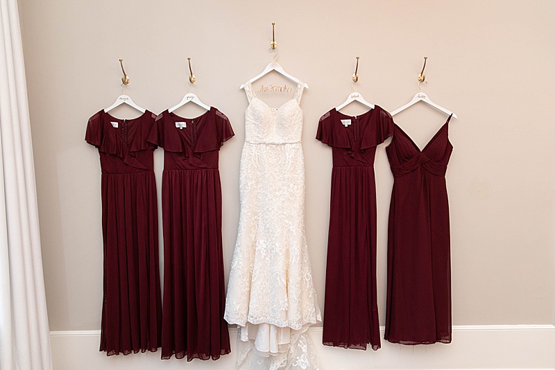 bride's dress hangs with burgundy bridesmaid gowns