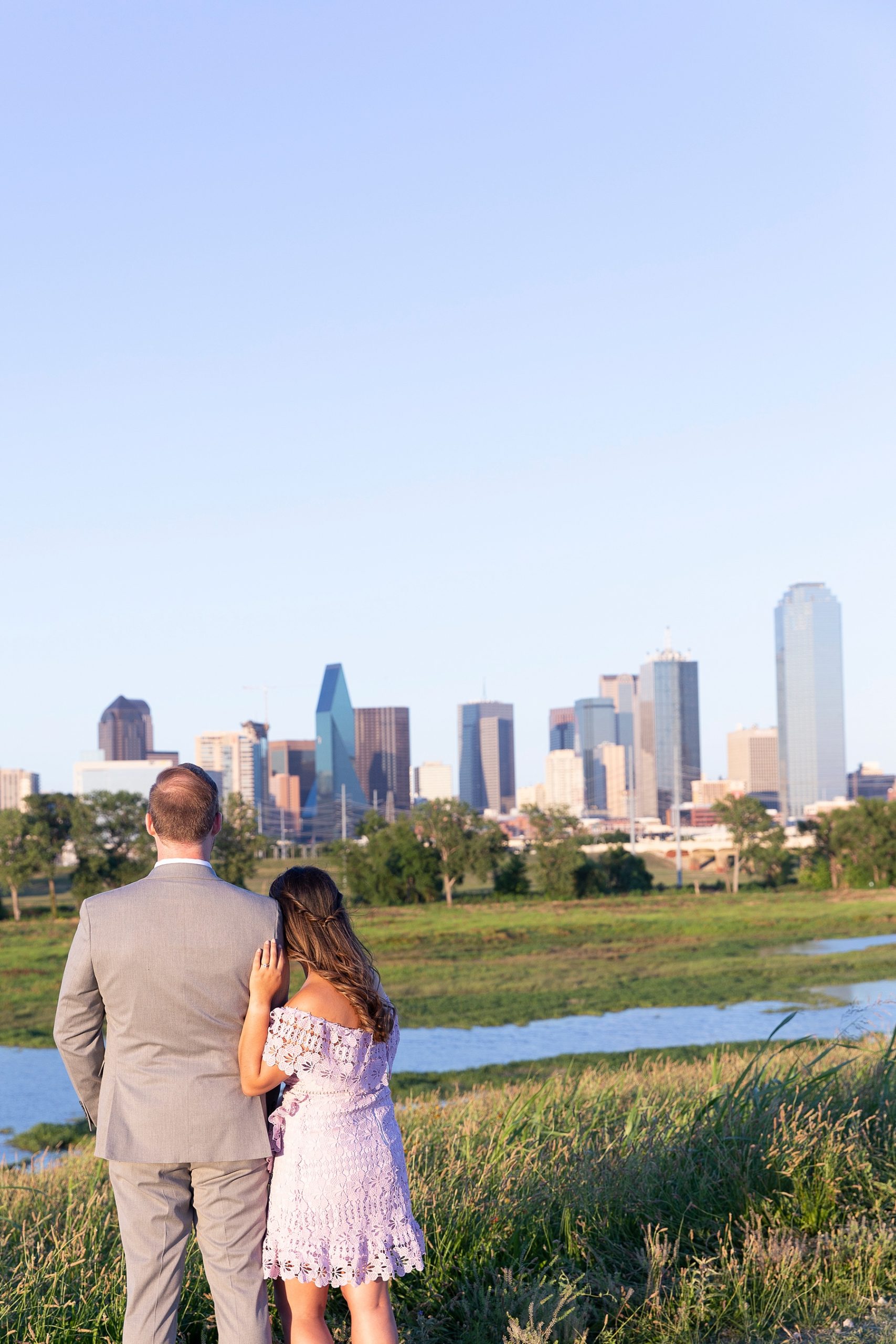 engaged couple looks at Dallas skyline from bridge