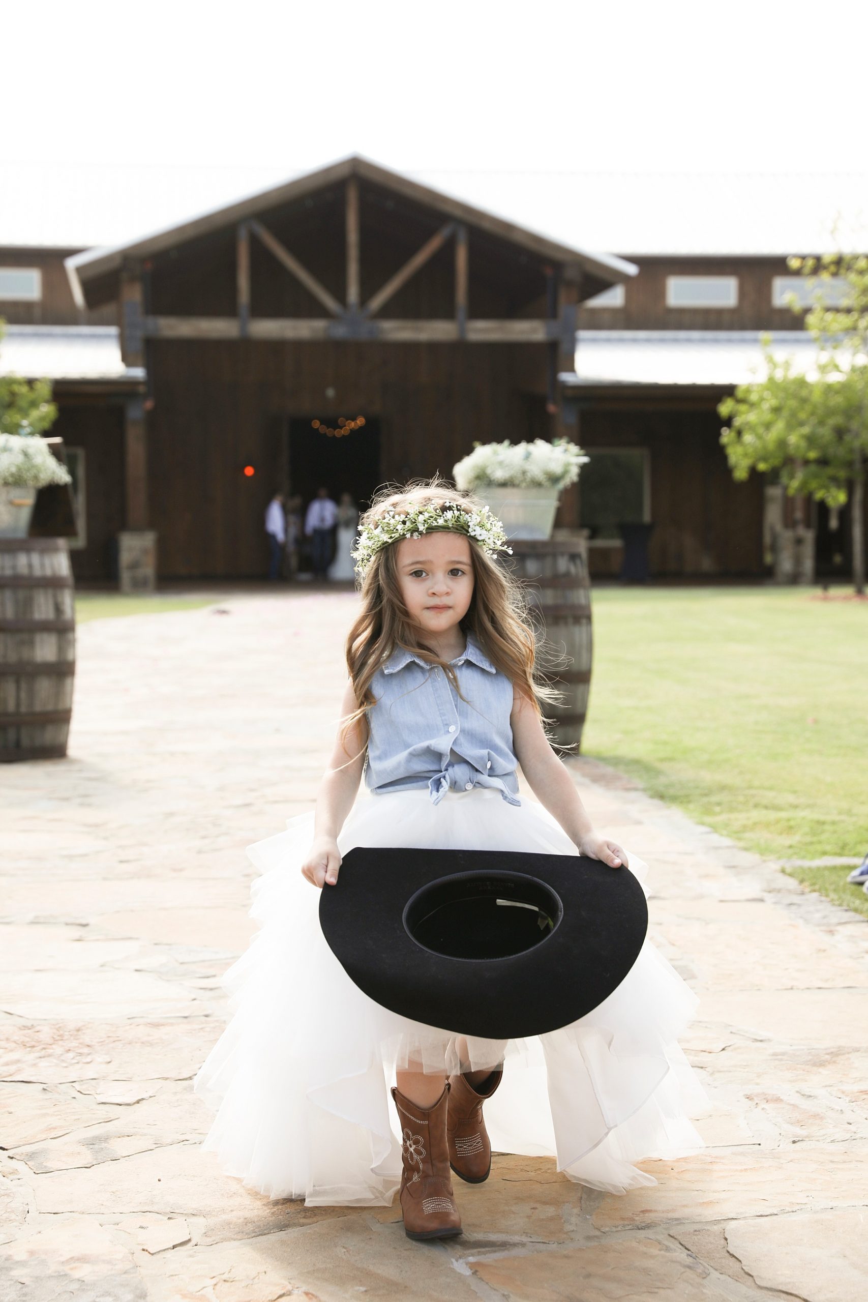flower girl walks down aisle carrying rancher hat at Lucky Spur Ranch