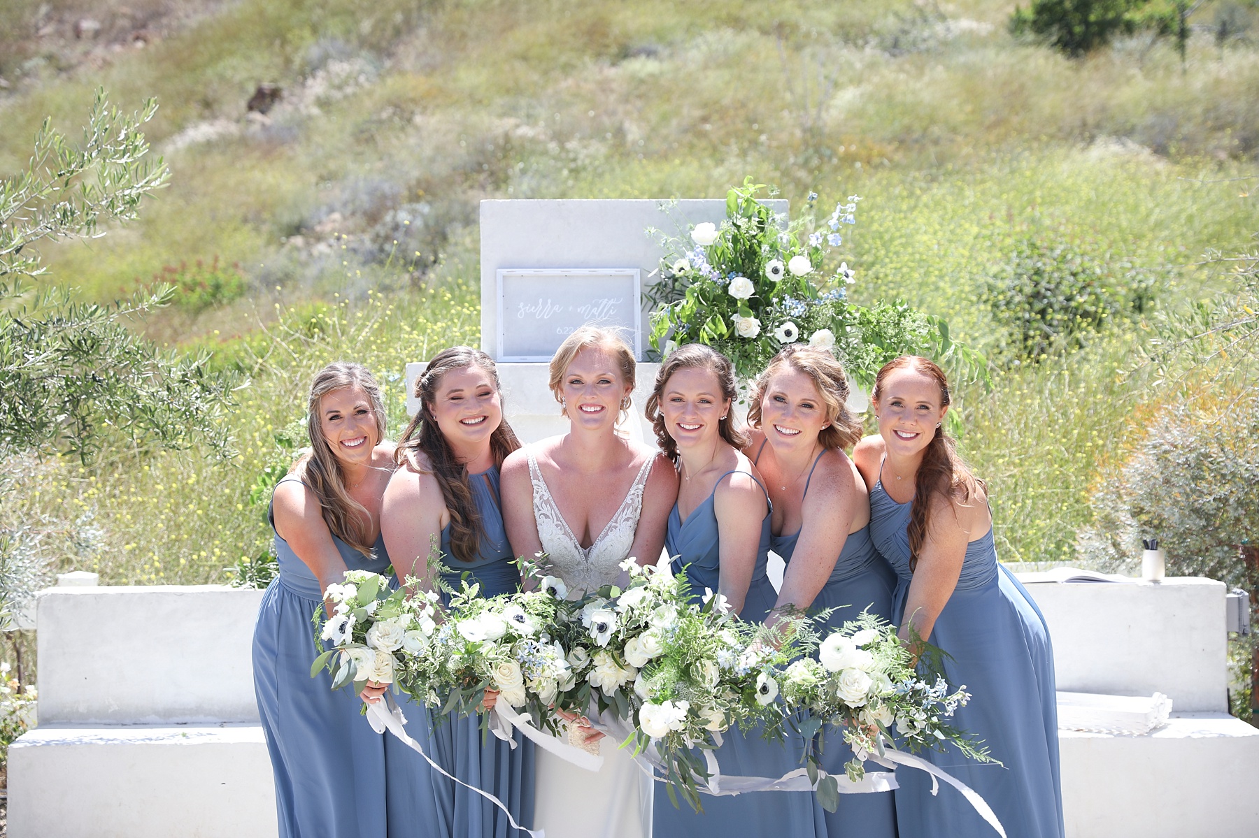 bridesmaids in blue gowns hold bouquets and lean into bride