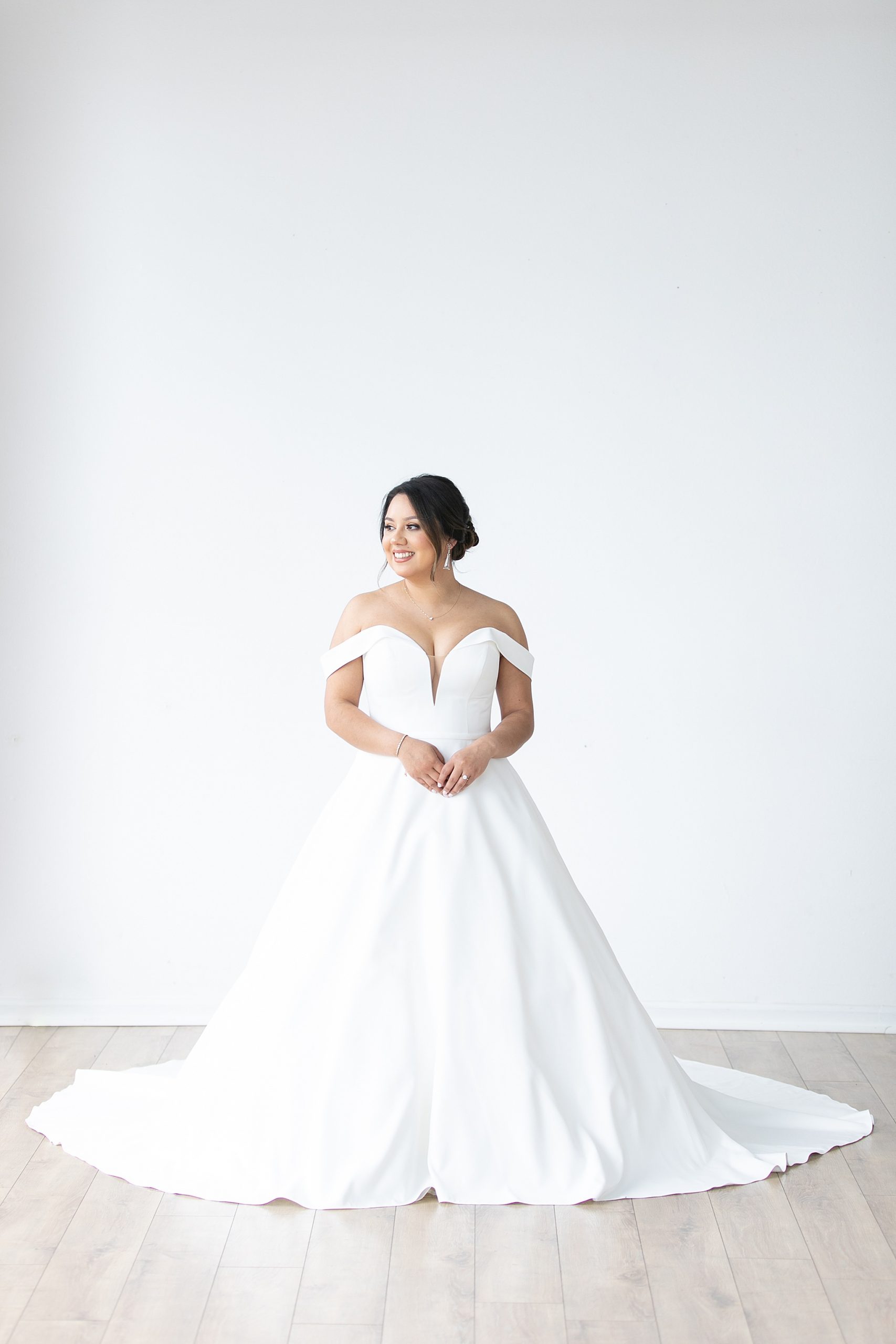 bride in modern wedding gown poses in front of white wall