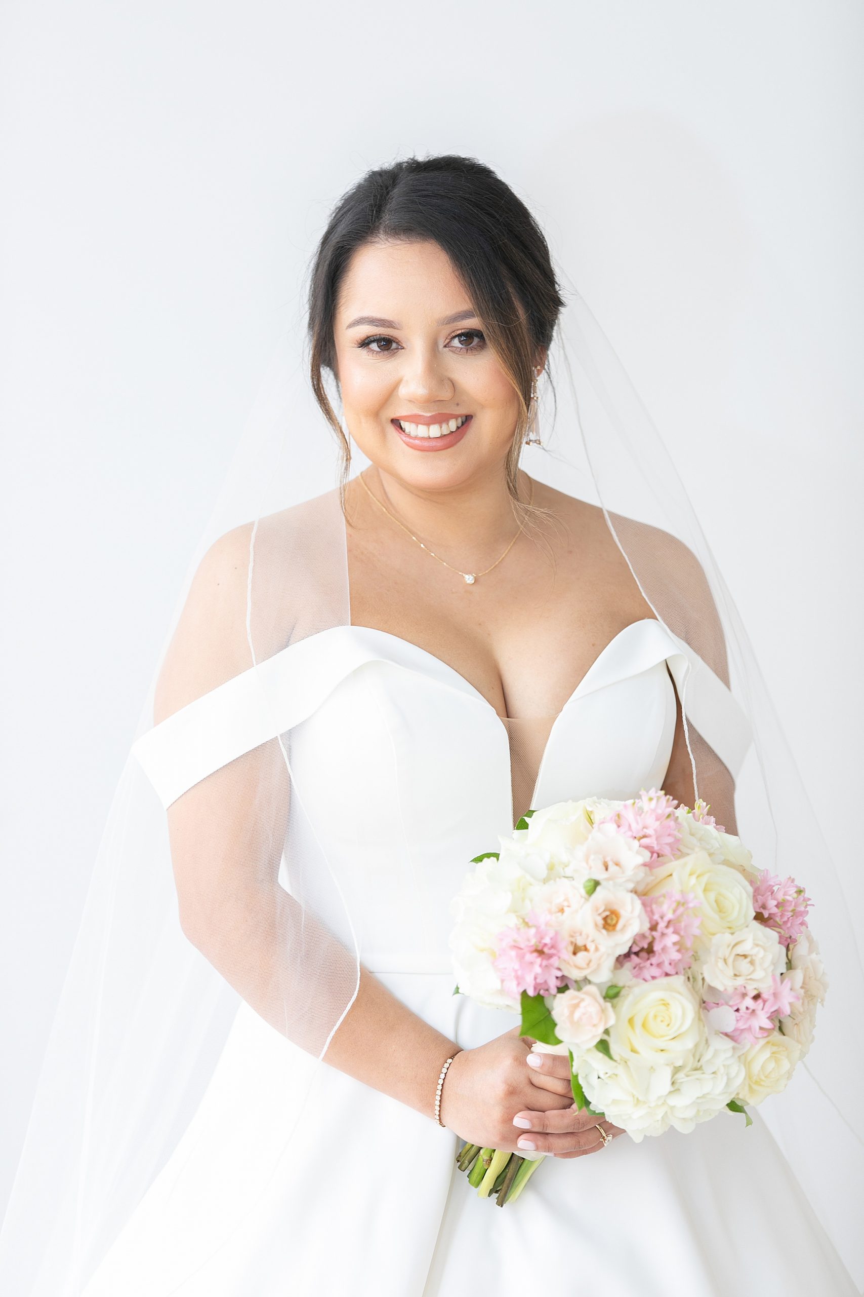 bride with veil holds bouquet of pink and ivory roses