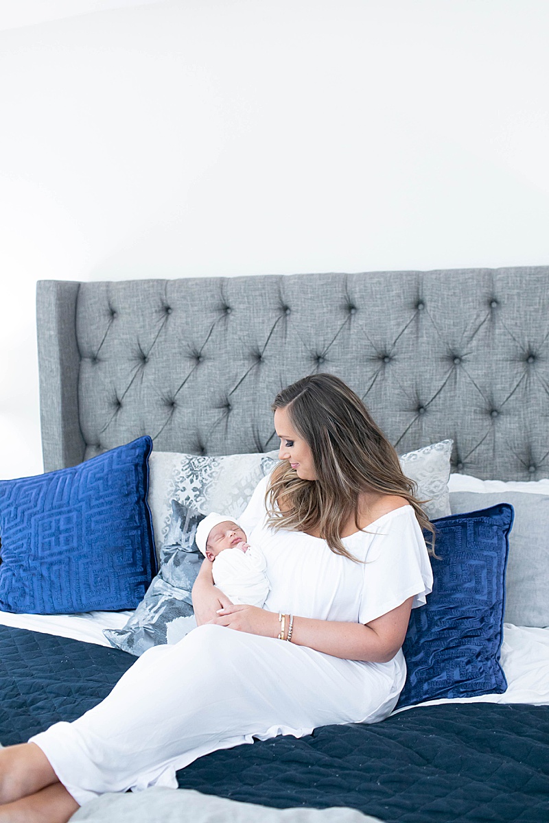 mom holds new baby boy snuggling on bed with blue pillows
