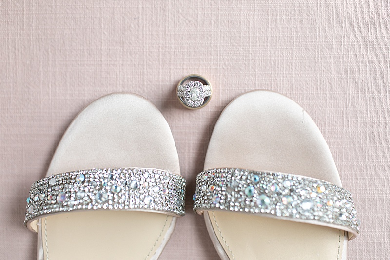 bride's shoes and rings on pink backdrop photographed by Randi Michelle Weddings