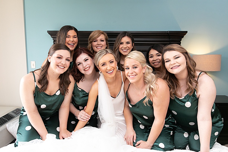 bride and bridesmaids in green polka dot PJs laugh on bed