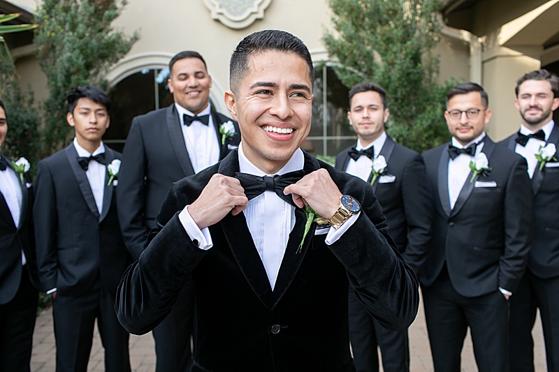 groom smiles while adjusting tie on velvet suit jacket