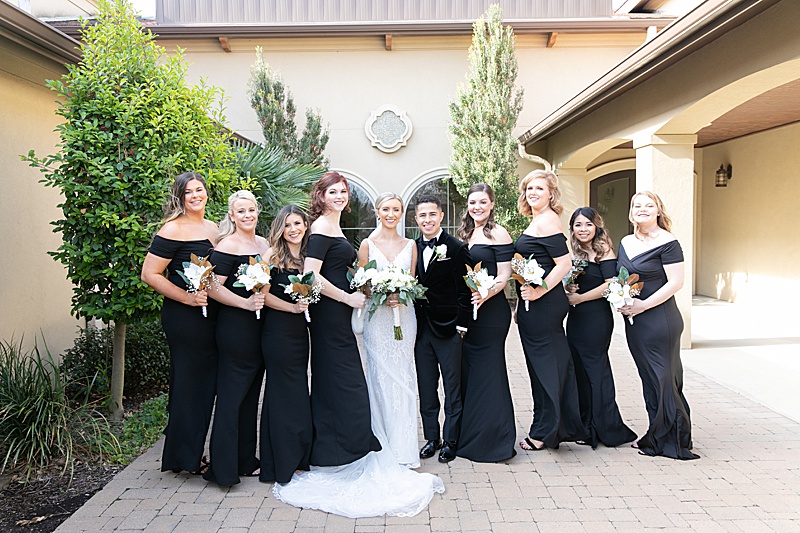 bridesmaids in black gowns pose with bride and groom