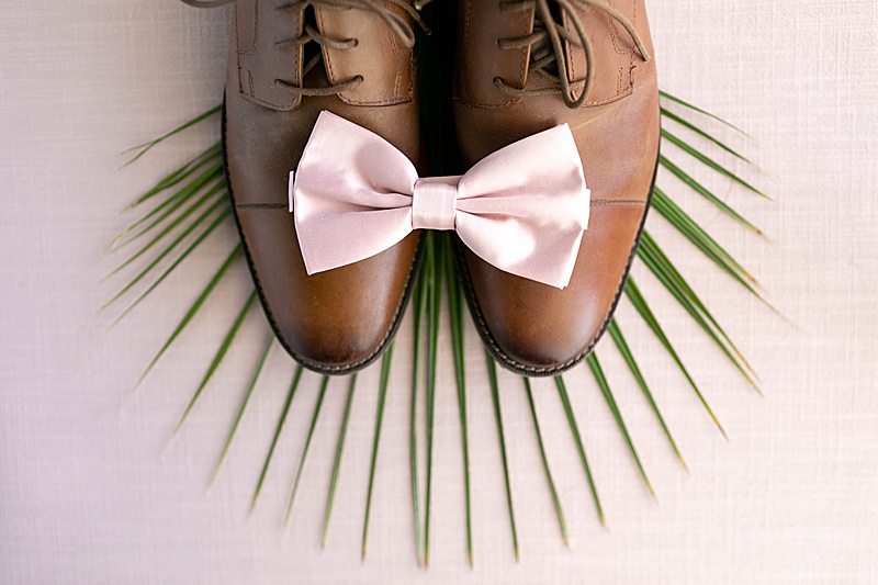 groom's tan shoes with pink bow on palm leaf and pink backdrop