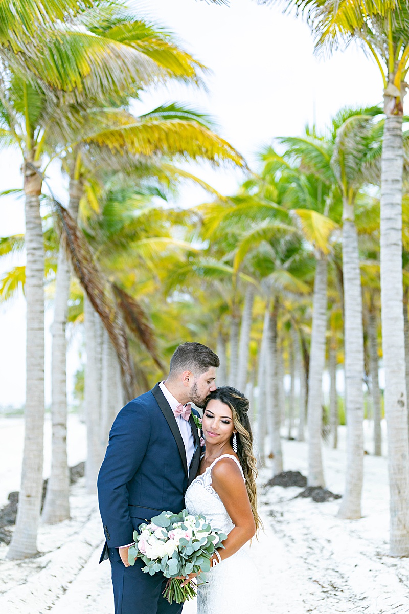 bride and groom pose under palm trees on beach
