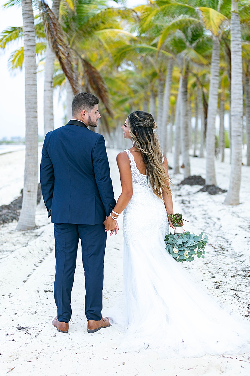 bride and groom hold hands and walk through palm trees