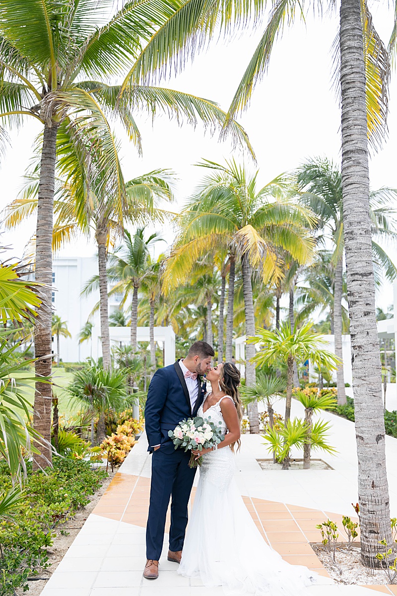 bride and groom kiss under palm trees in Mexico