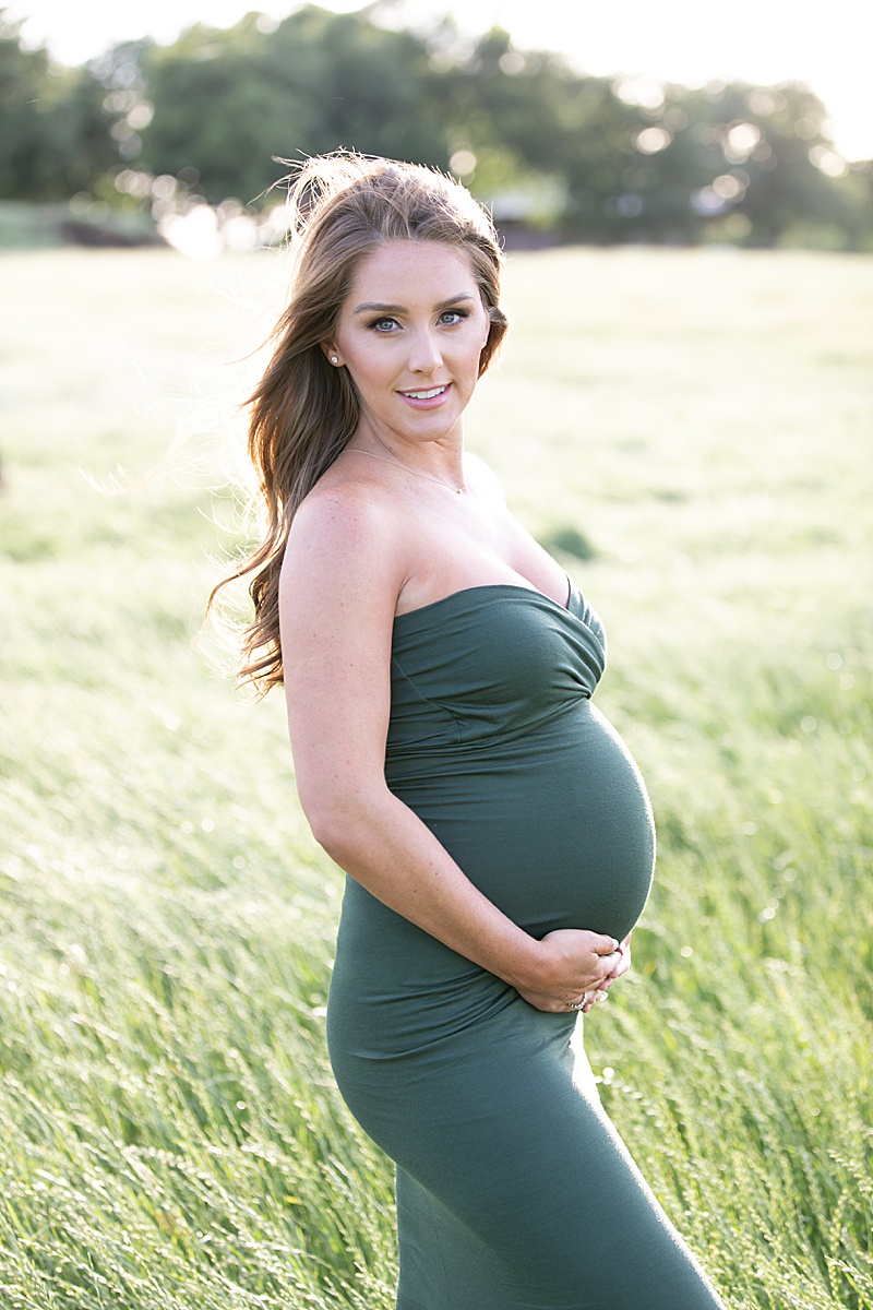mom in green gown holds baby belly during TX maternity portraits