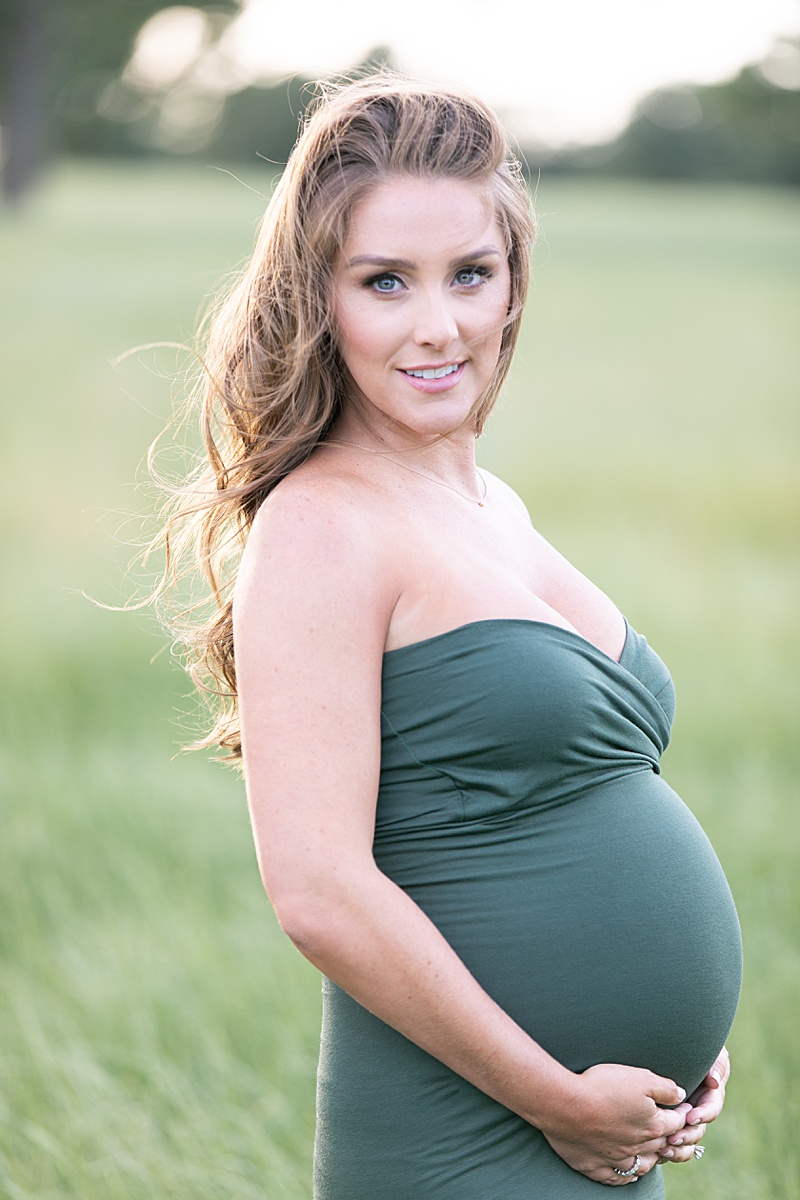 mom in green gown holds baby belly during maternity session