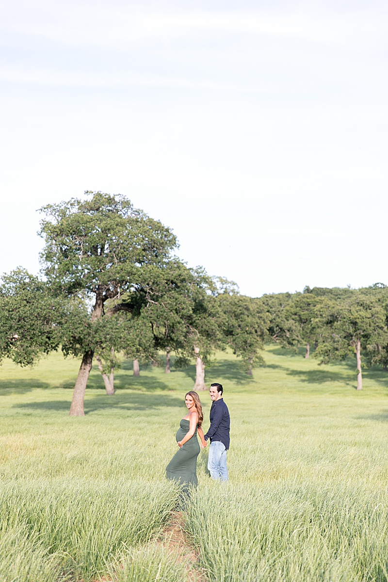 parents-to-be walk through field during Summer Maternity Portraits