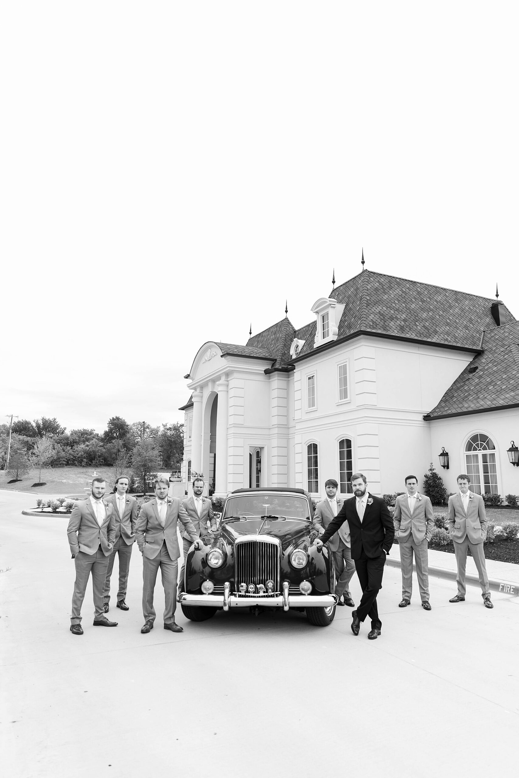 groom and groomsmen lean on front of classic car outside the Hillside Estate
