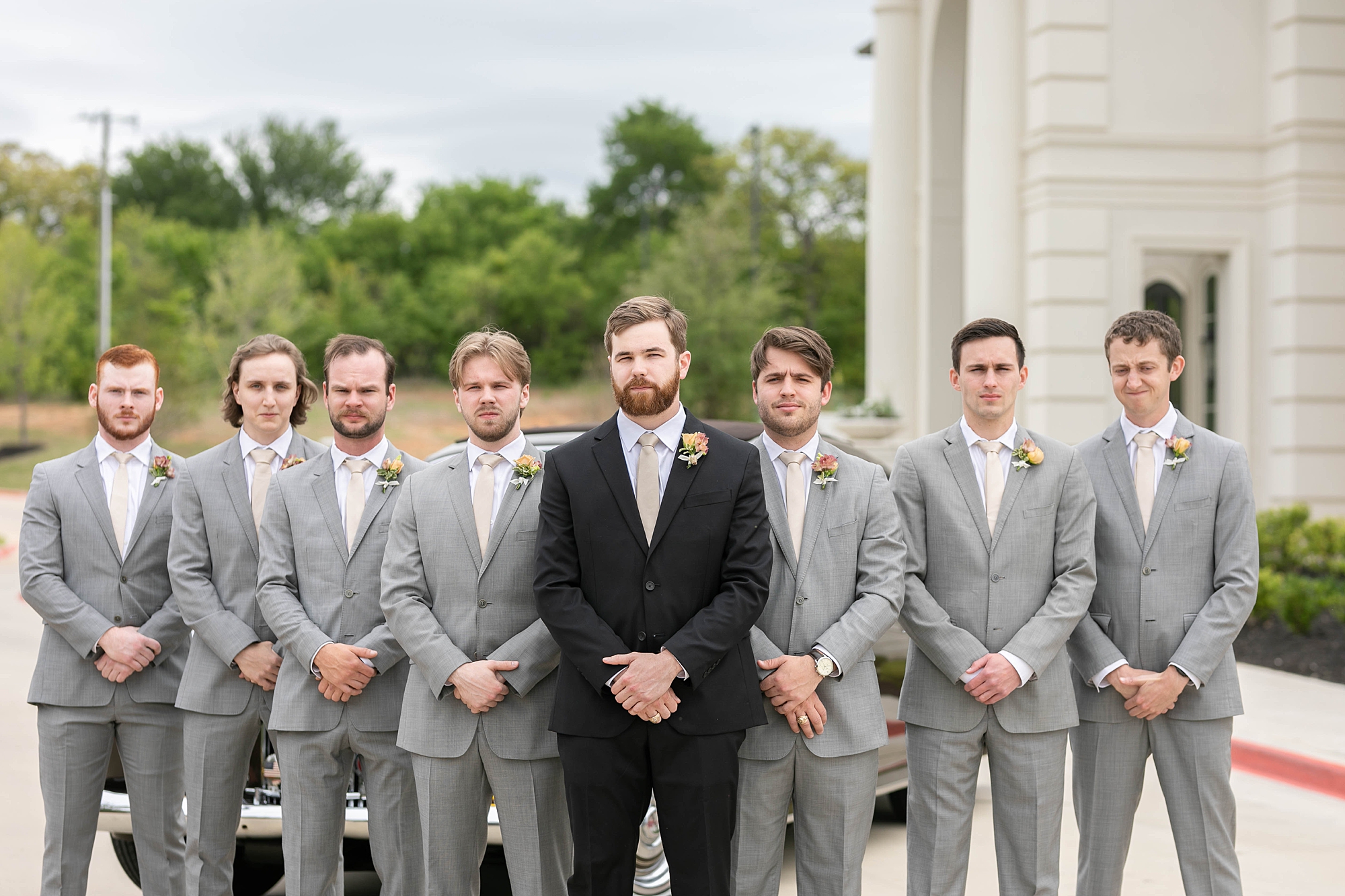 groom in black suit stands with groomsmen in grey suits 