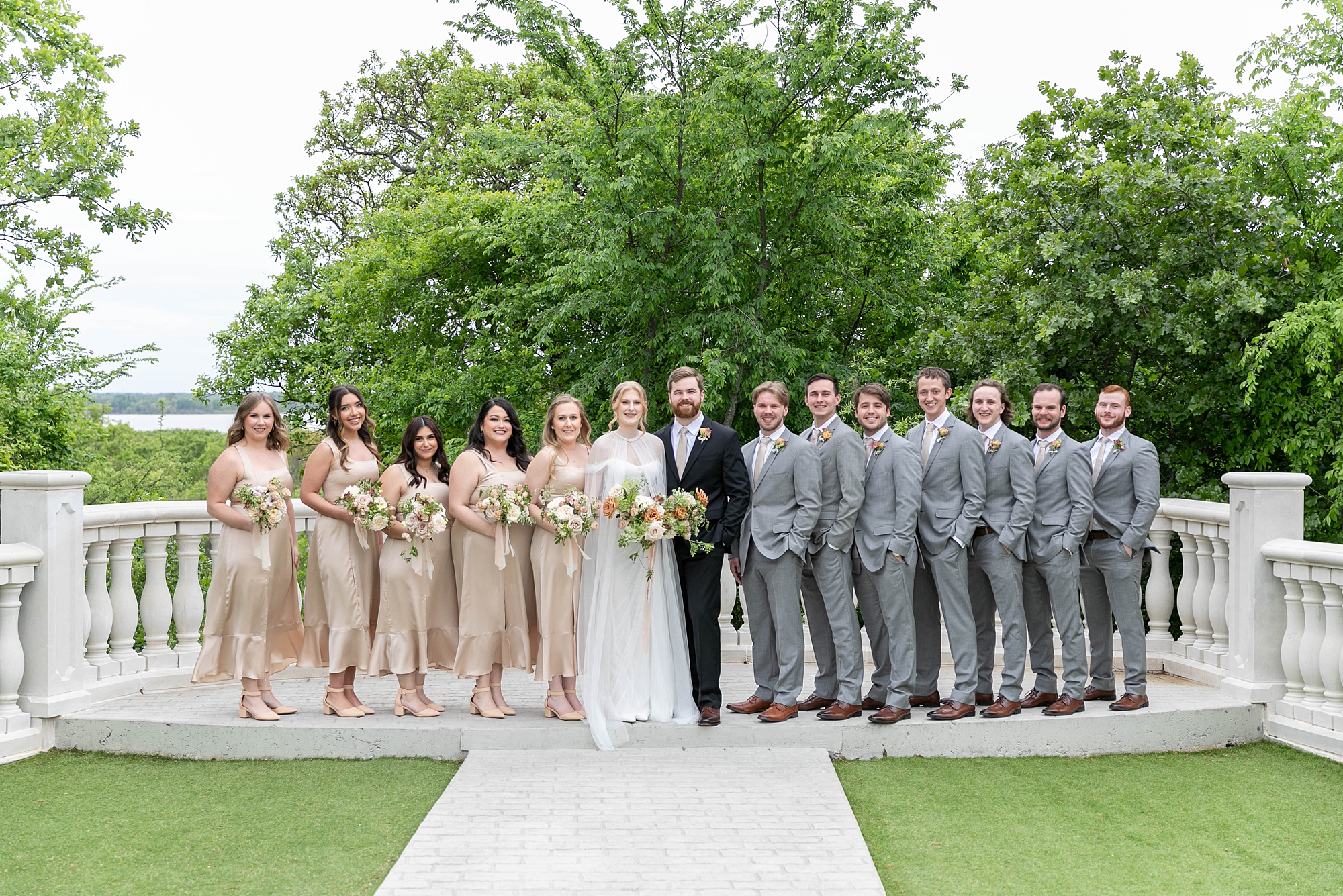 bride and groom stand on patio at the Hillside Estate with wedding party around them in grey and champagne attire 