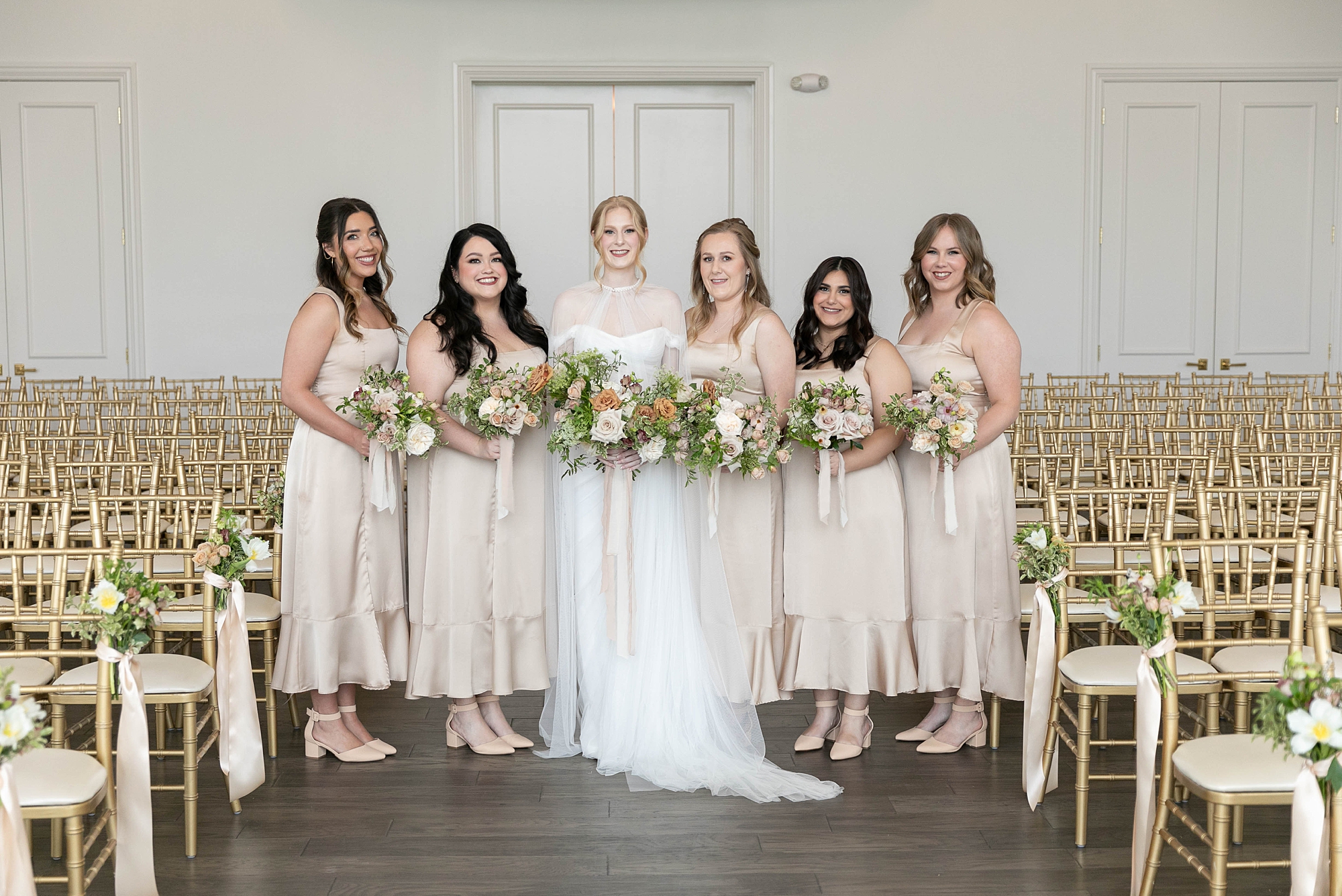 bride stands with bridesmaids in pale gowns with bouquets of muted roses 