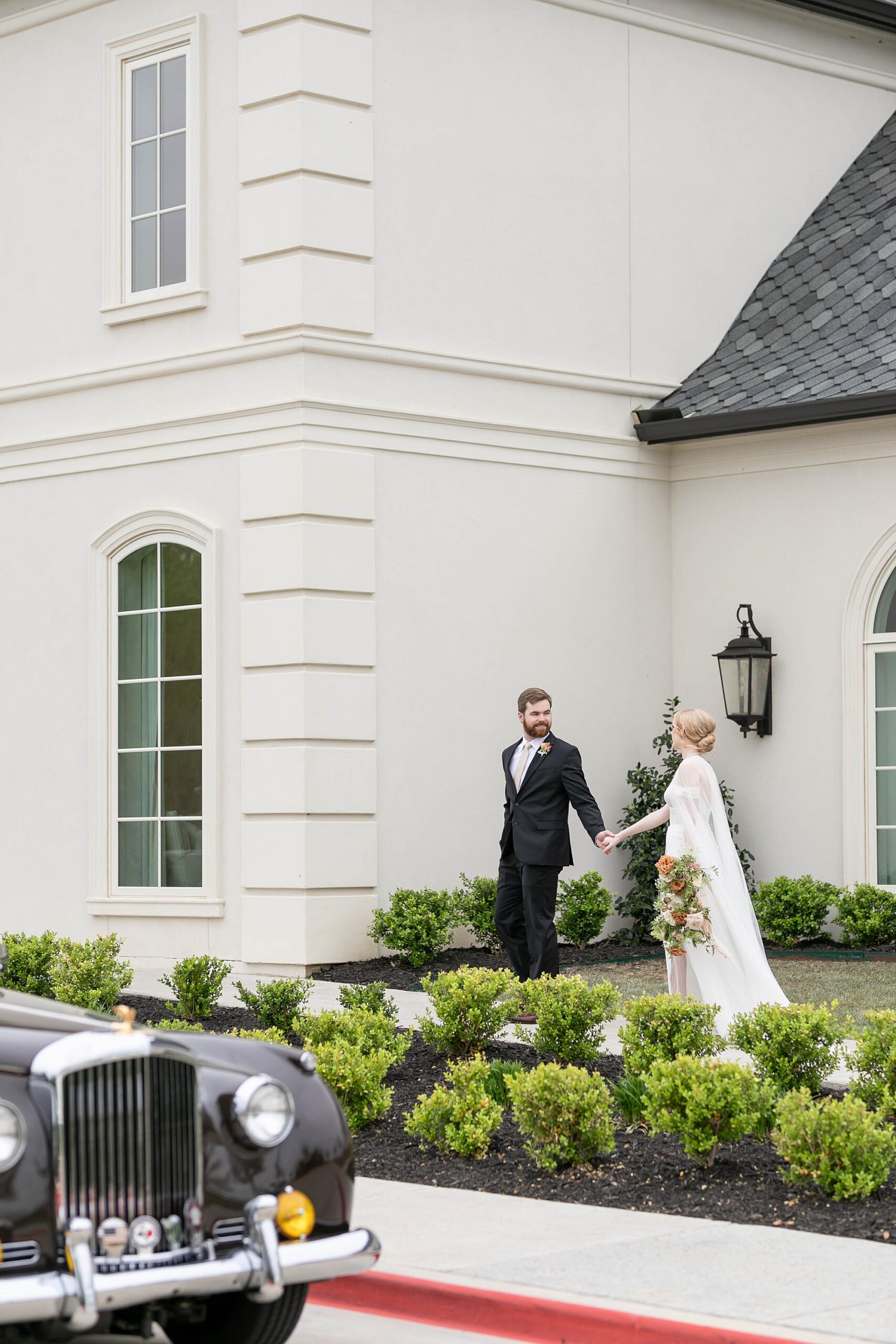 groom leads bride along sidewalk outside the Hillside Estate