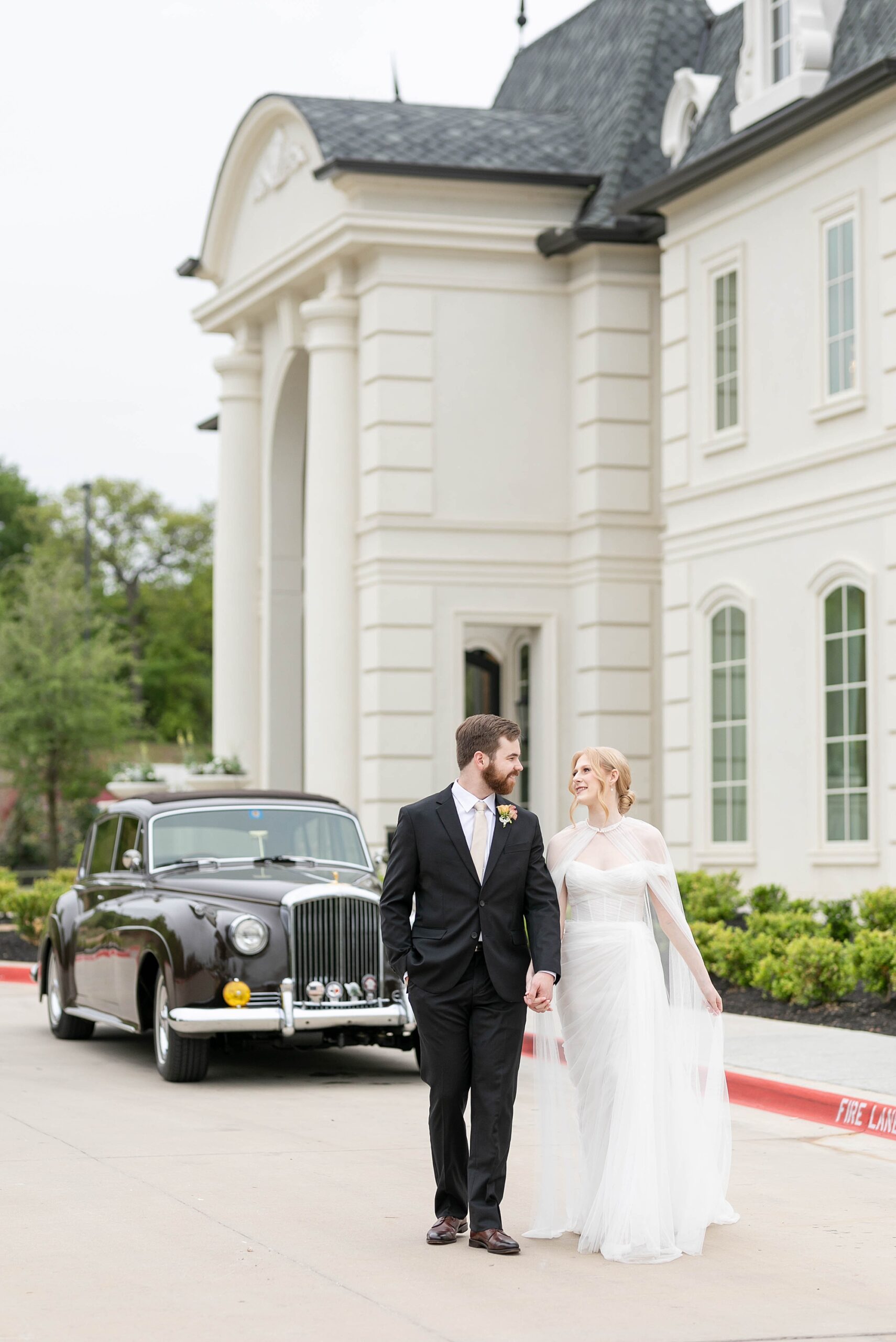 bride and groom hold hands walking in front of black car outside the Hillside Estate