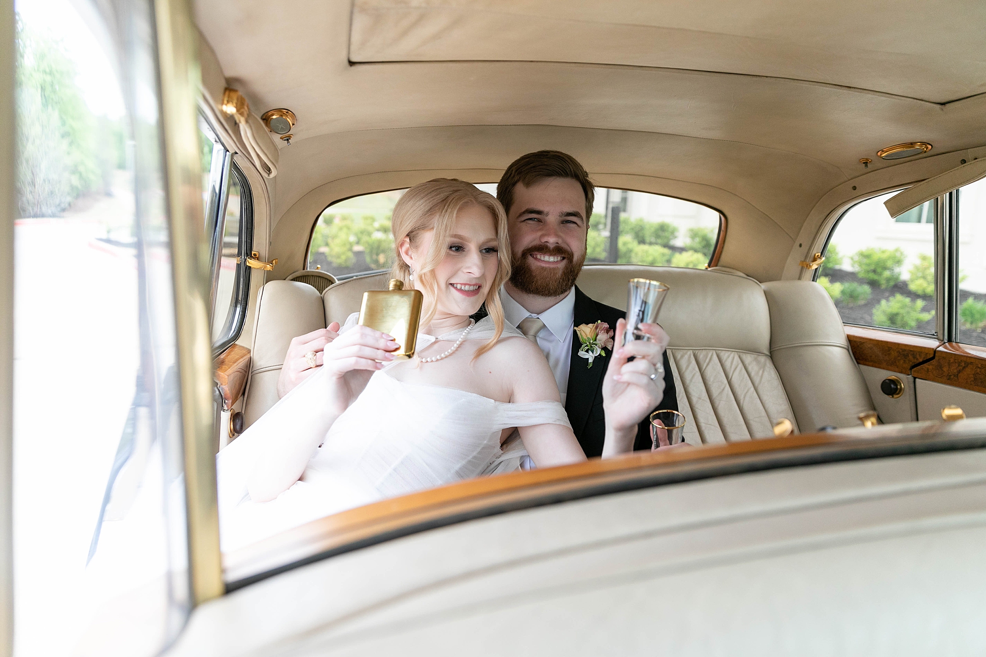 bride and groom toast champagne in the back of a classic car on wedding day