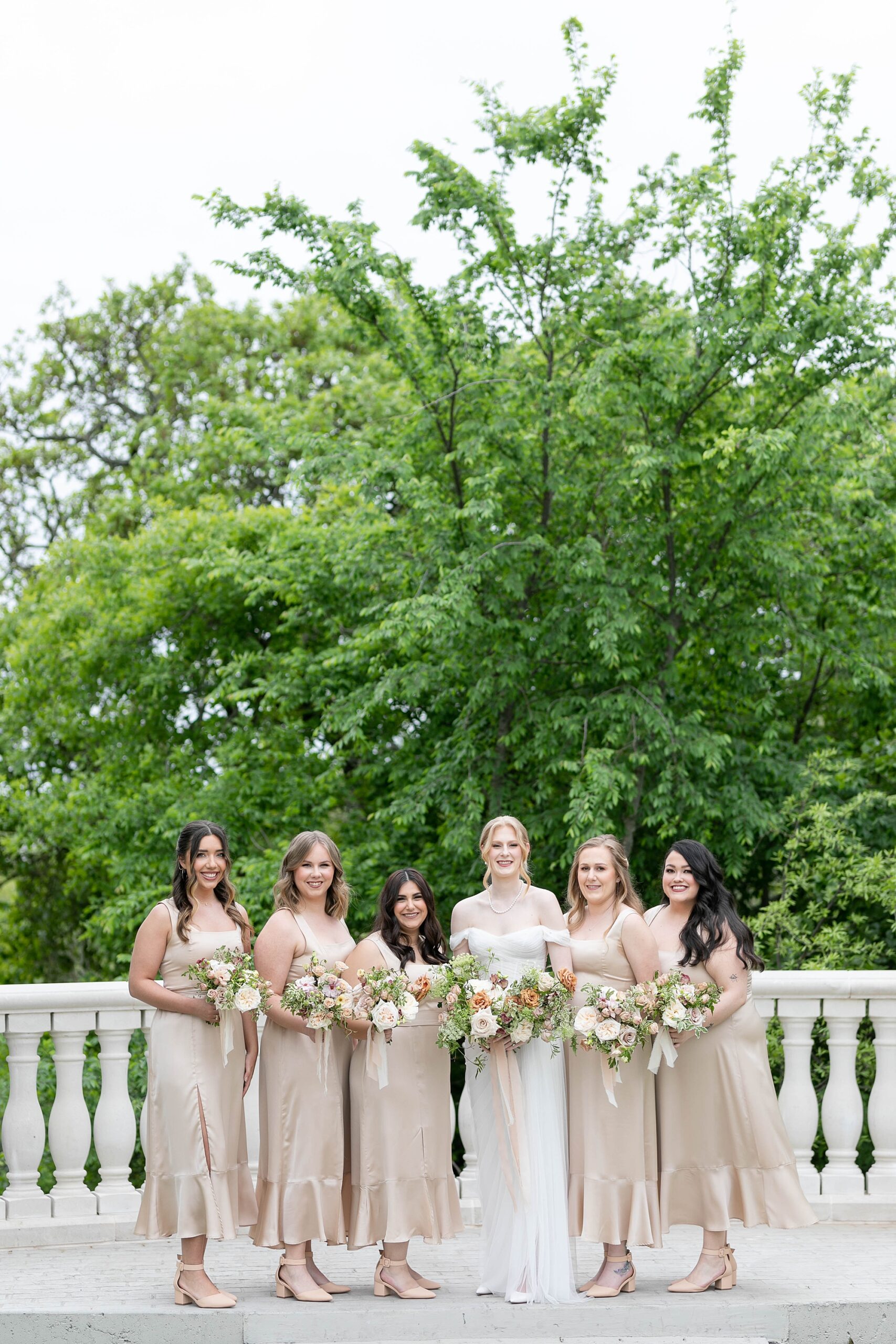 bride poses with bridesmaids in champagne gowns on patio at the Hillside Estate