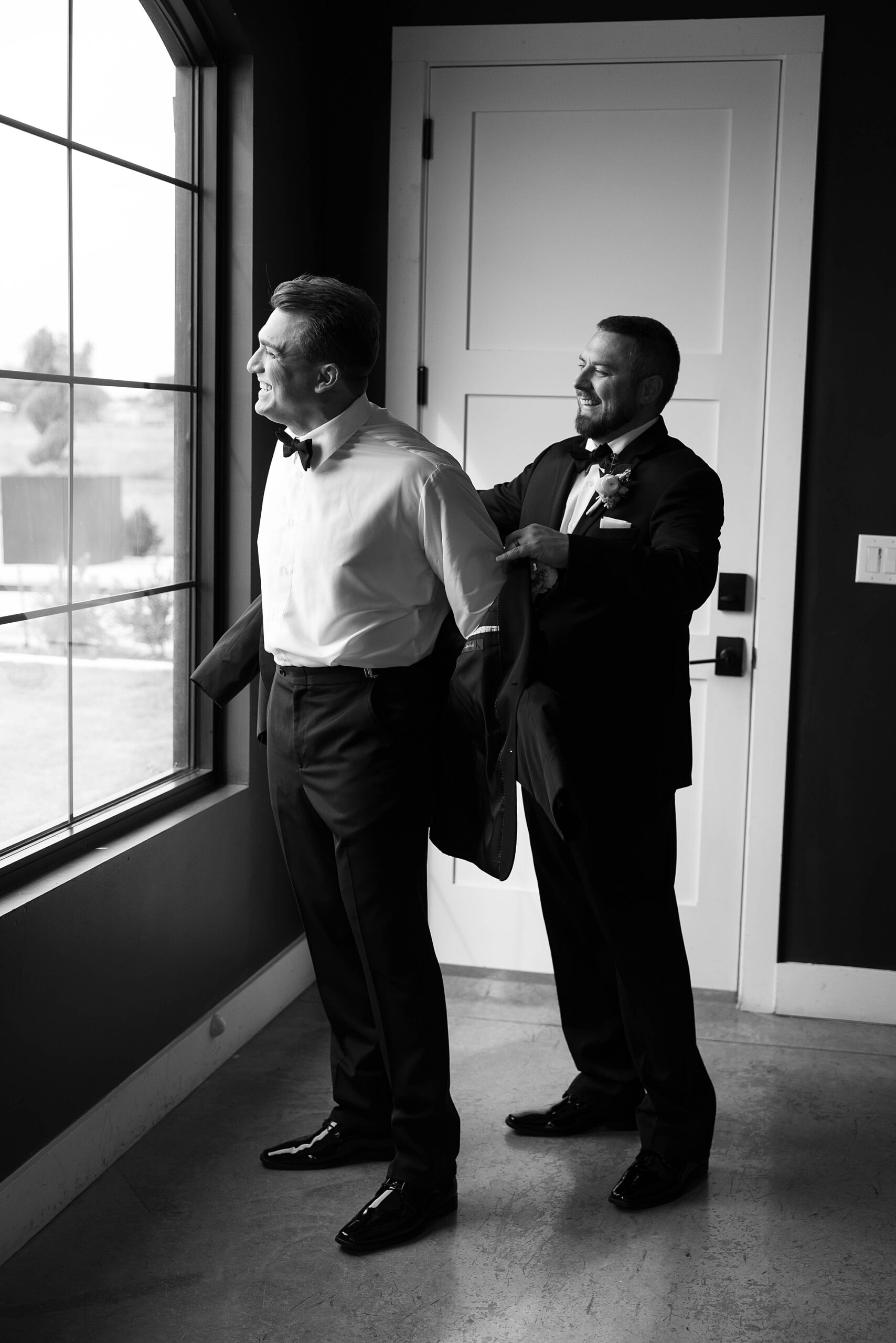 groomsman helps groom into jacket on wedding morning in Dallas TX