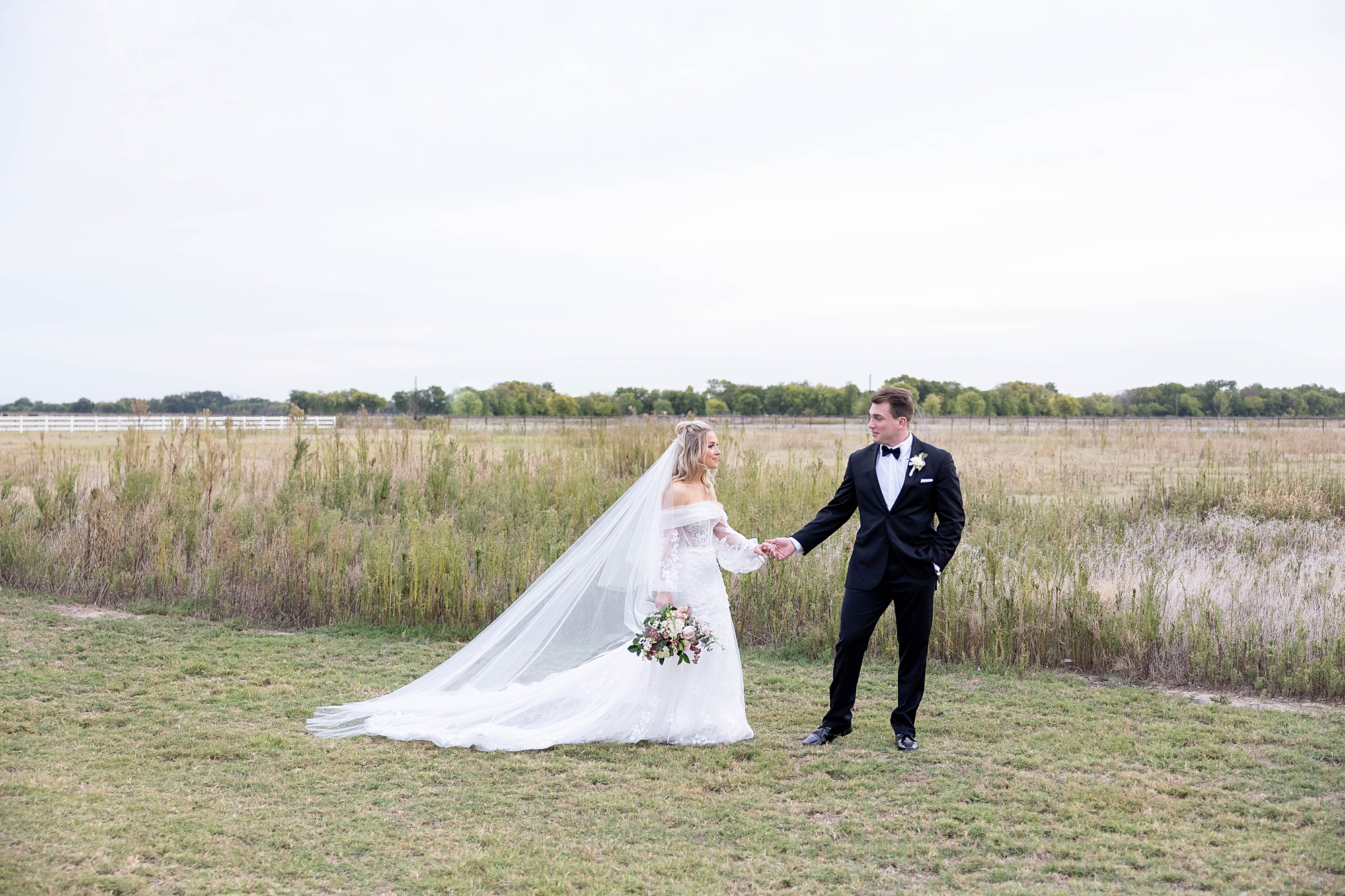 newlyweds hold hands walking along field at the Gardenia