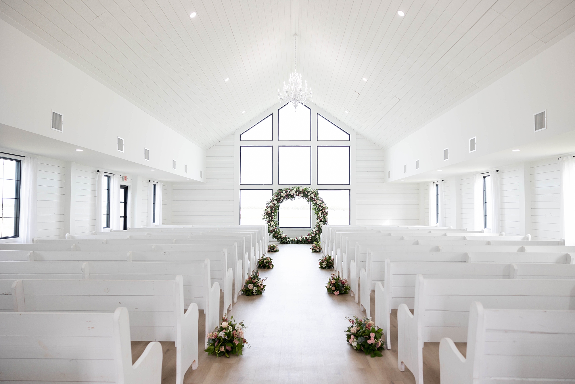 ceremony setup inside chapel at the Gardenia with white pews and flowers lining aisle 