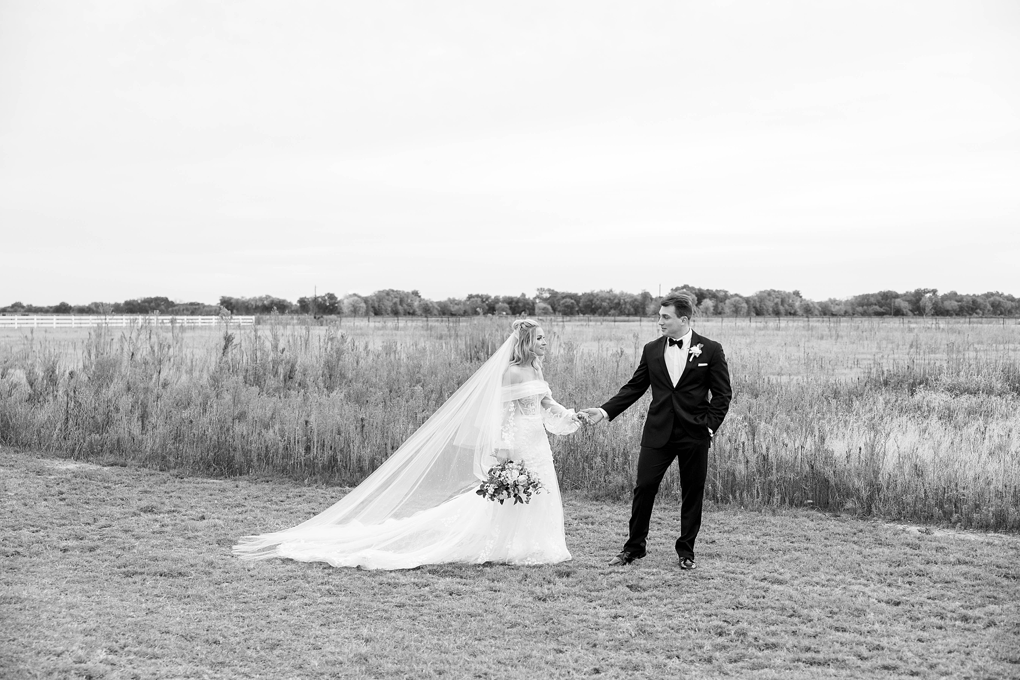 black and white photo of bride and groom walking near field at the Gardenia