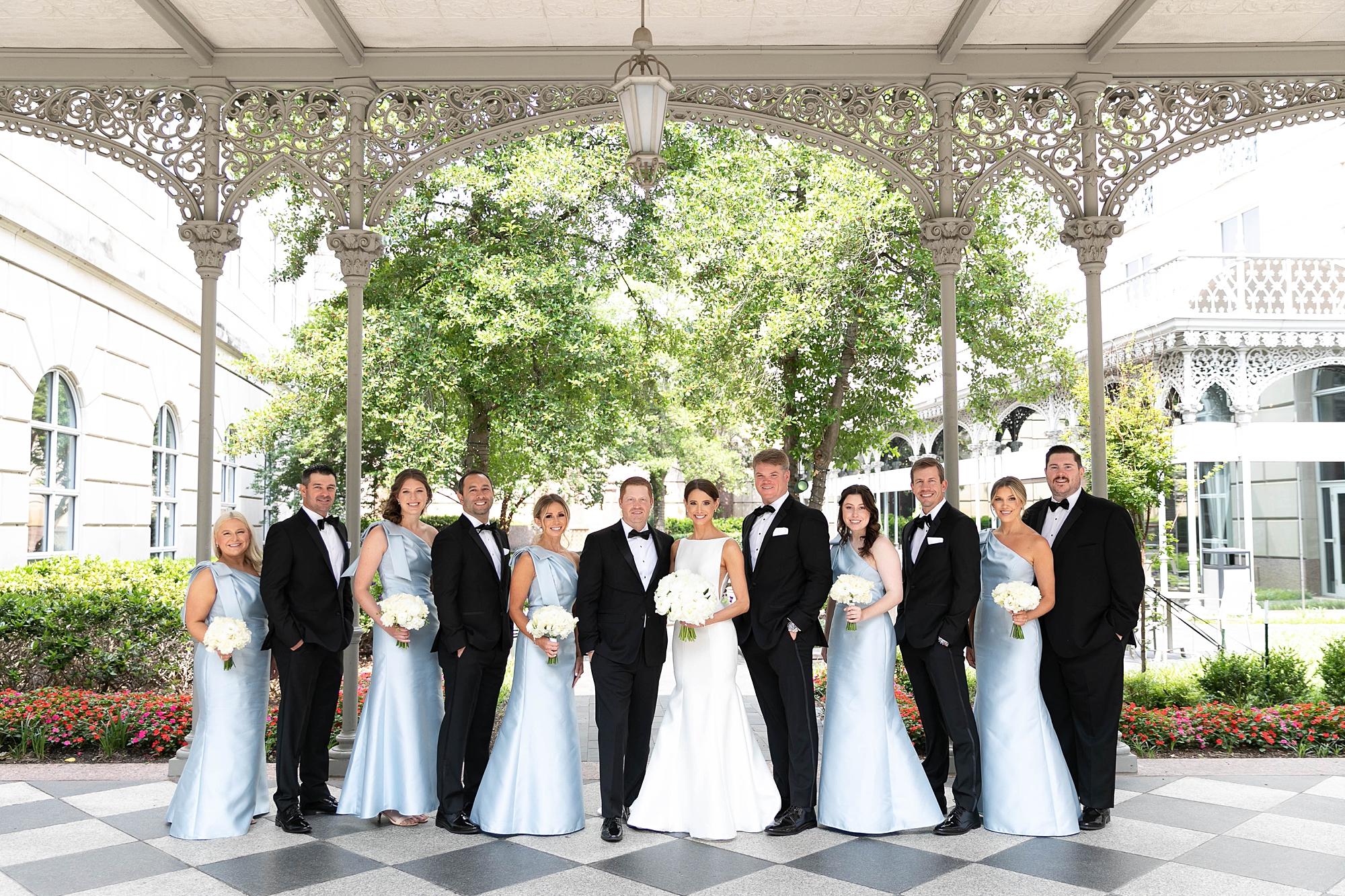 bride and groom pose with wedding party in light blue gowns and black suits outside the Hotel Crescent Court