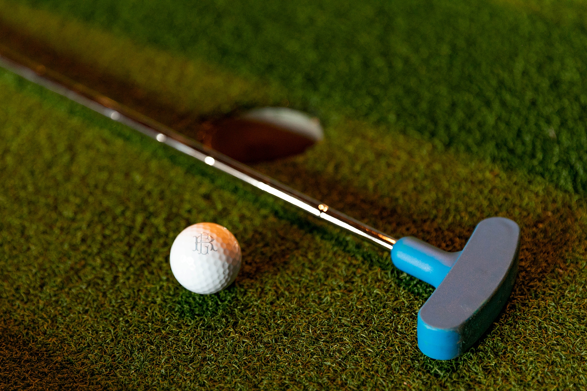 putter lays on green with golf ball and hole for wedding reception