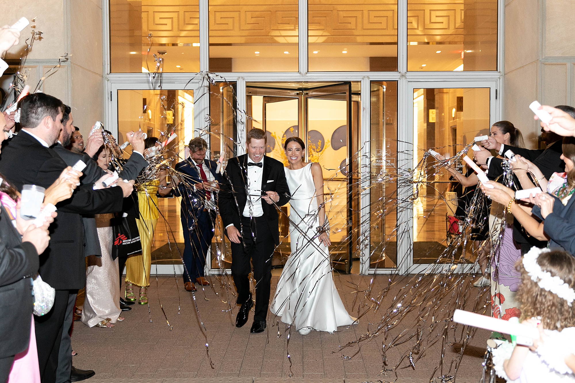bride and groom laugh leaving wedding reception through streamer exit