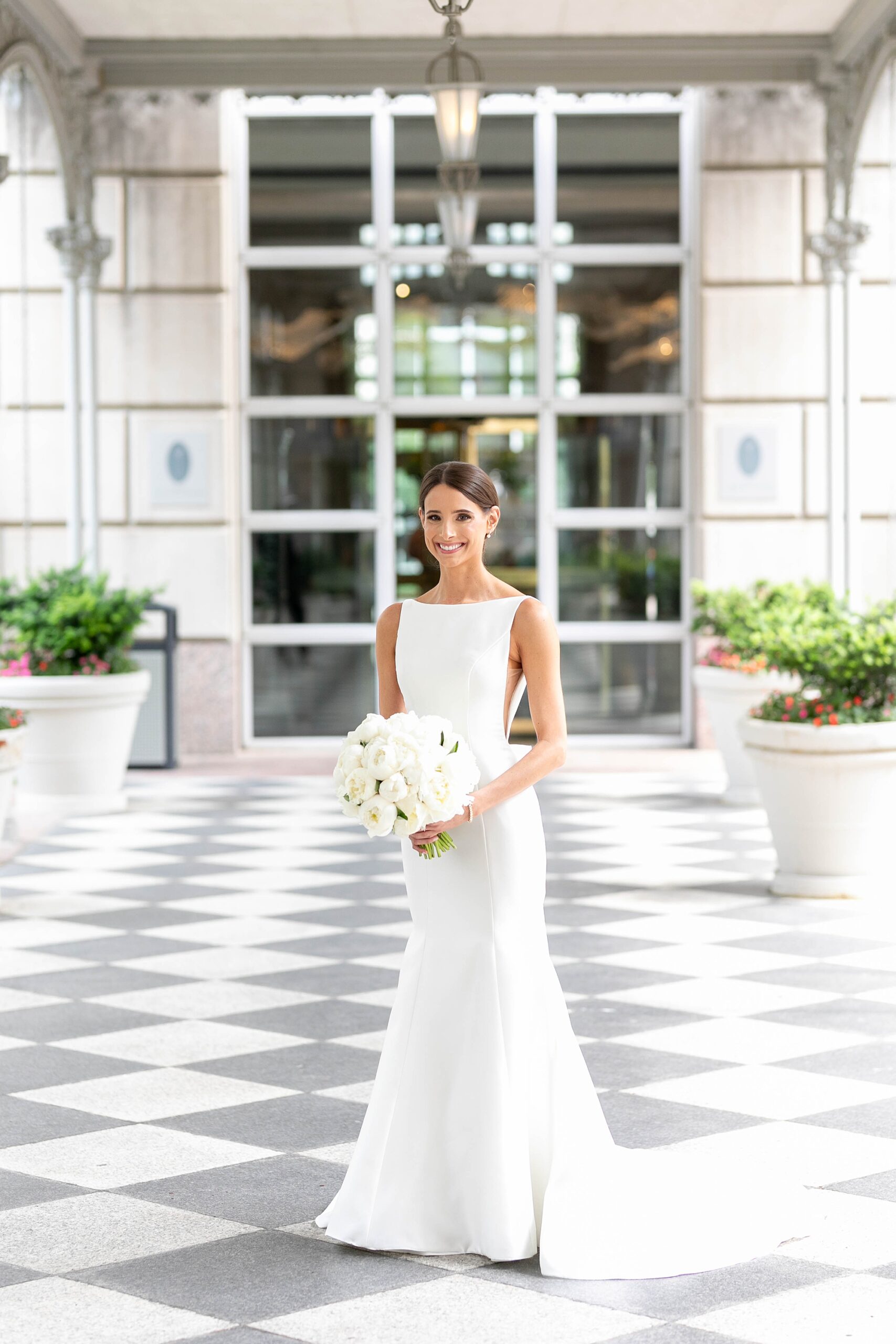 bride stands outside the Hotel Crescent Court holding bouquet of white roses 