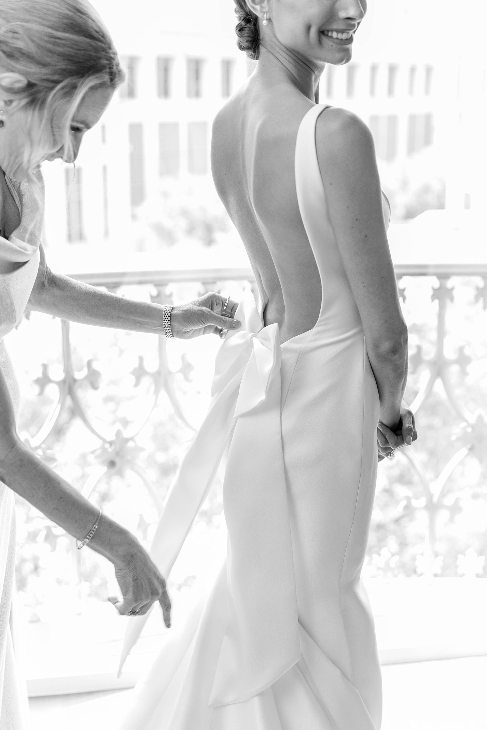 bridesmaid adjusts bow on back of wedding dress for bride 