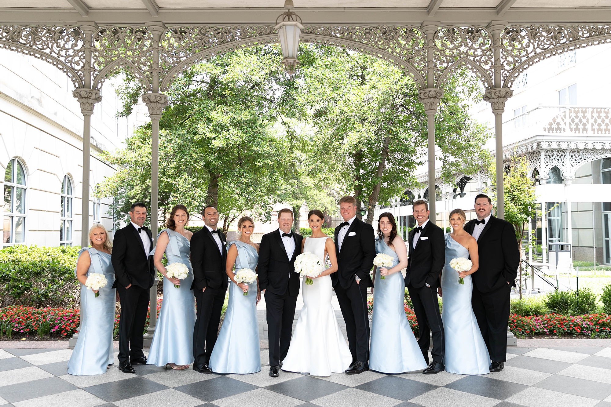 bride and groom stand with wedding party in blue dresses and black suits 