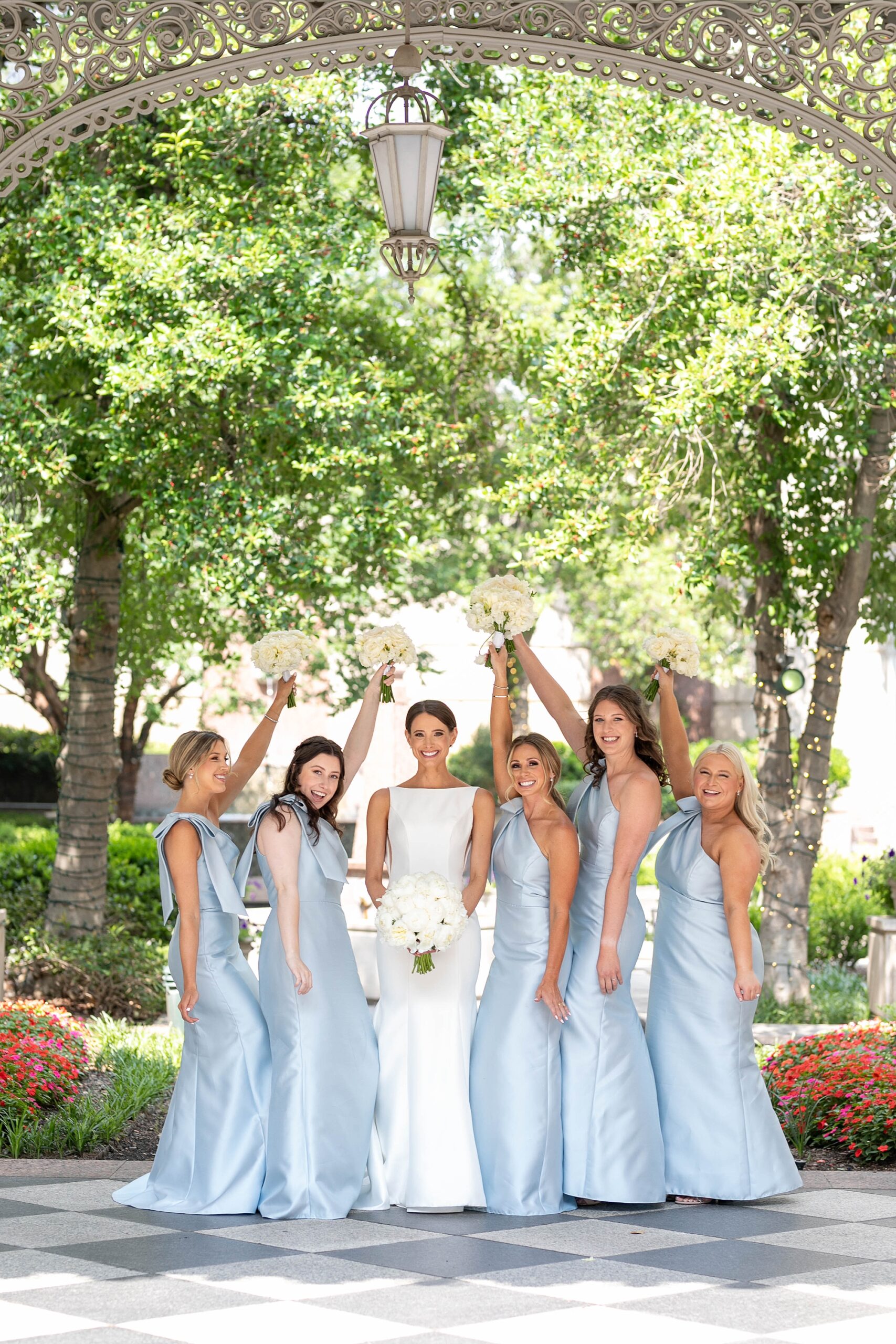 bride cheers with bridesmaids in light blue gowns holding bouquets of white roses 