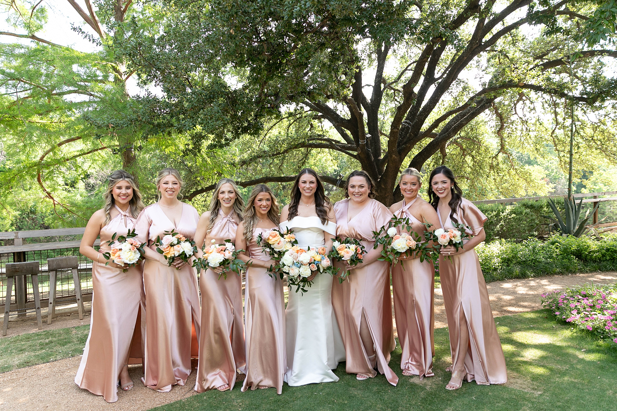 bride stands with bridesmaids in satin pink gowns 