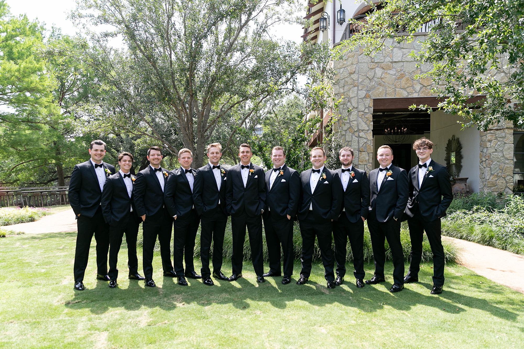 groom and groomsmen in  black suits stand on lawn at the Hotel Drover