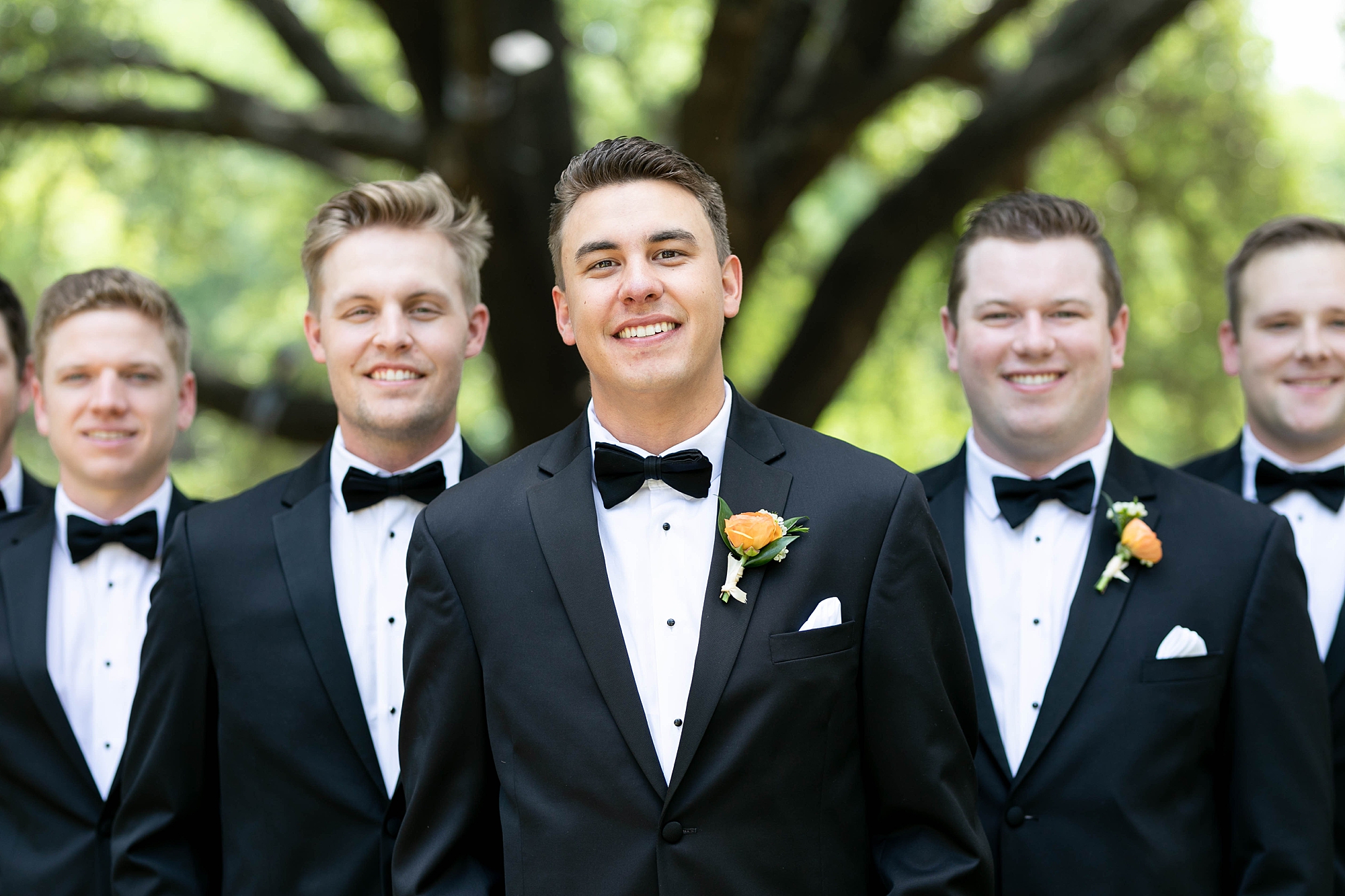 groom stands with groomsmen in black ties and black tuxes  