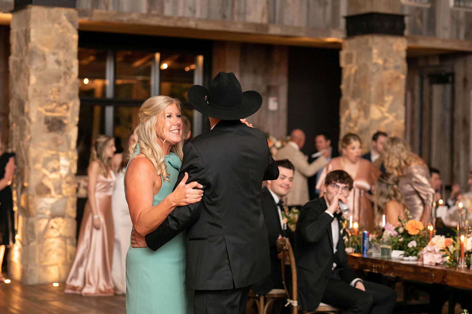 groom in cowboy hat dances with mom during wedding reception in the barn at the Hotel Drover