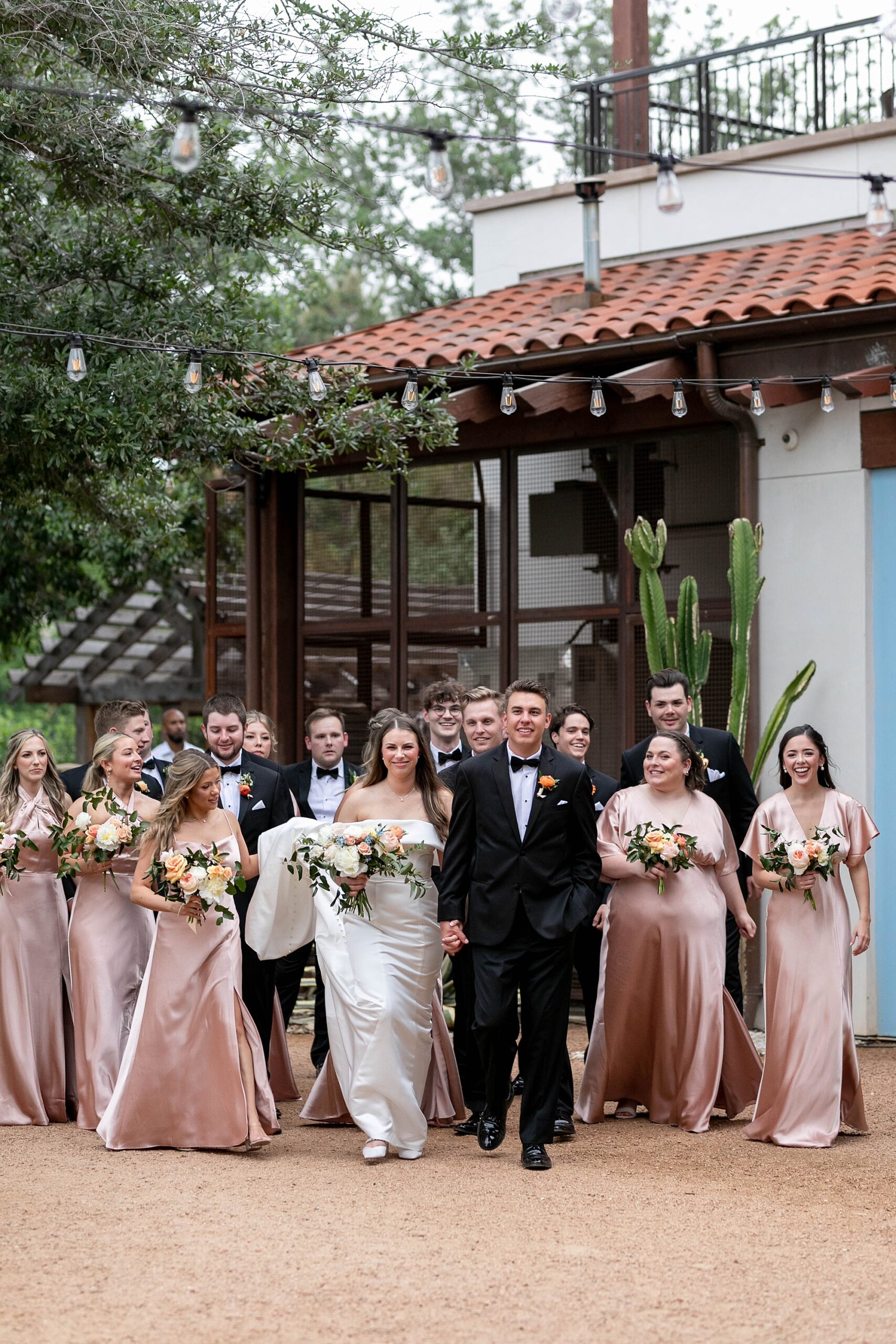 bride and groom walk with wedding party in pink dresses and black suits 