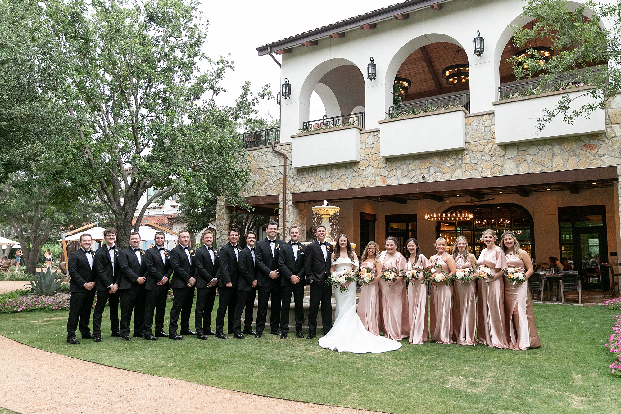 bride and groom stand with wedding party in black suits and pink gowns 