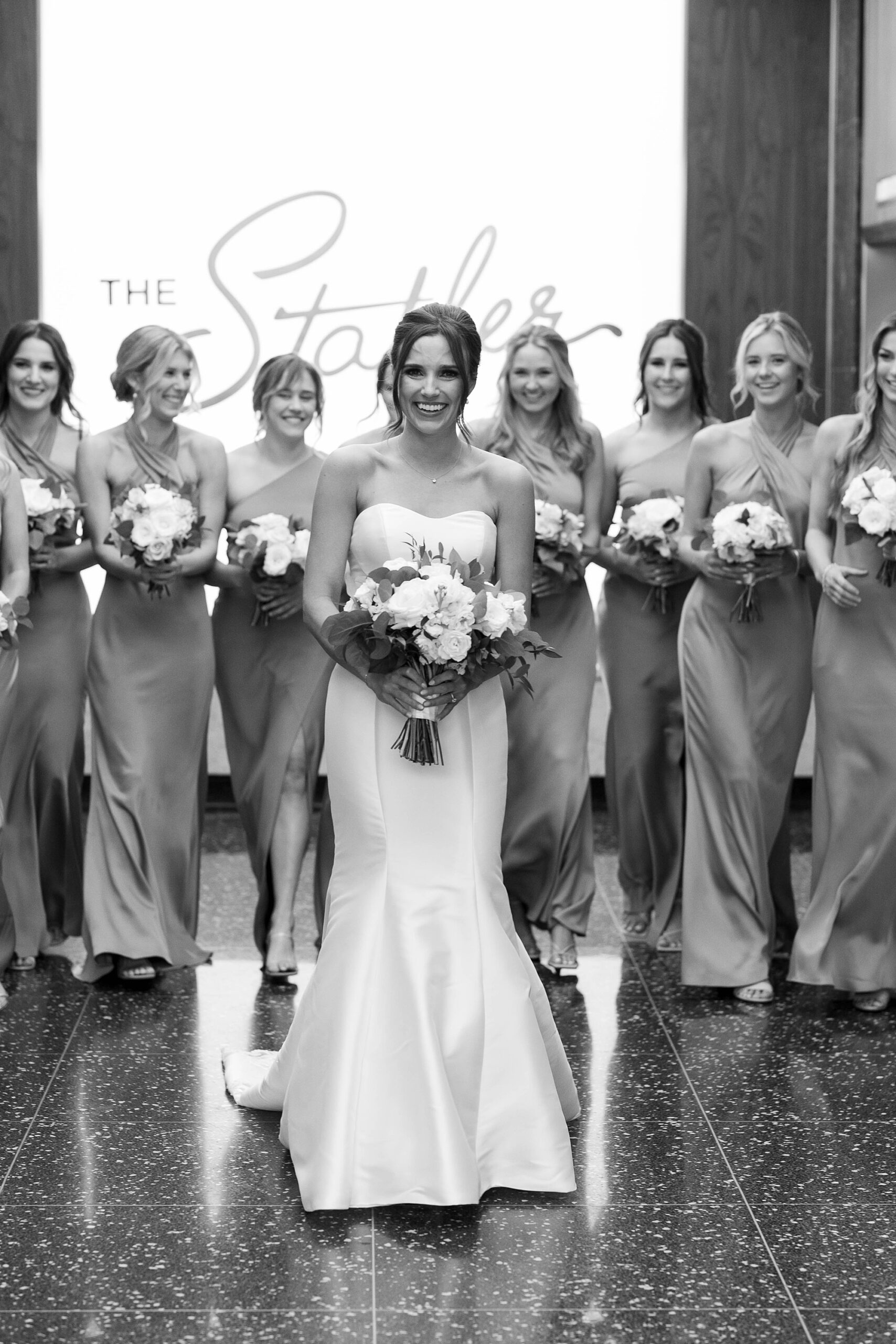 bride stands slightly in front of bridesmaids holding bouquets of white flowers at the Statler Hotel