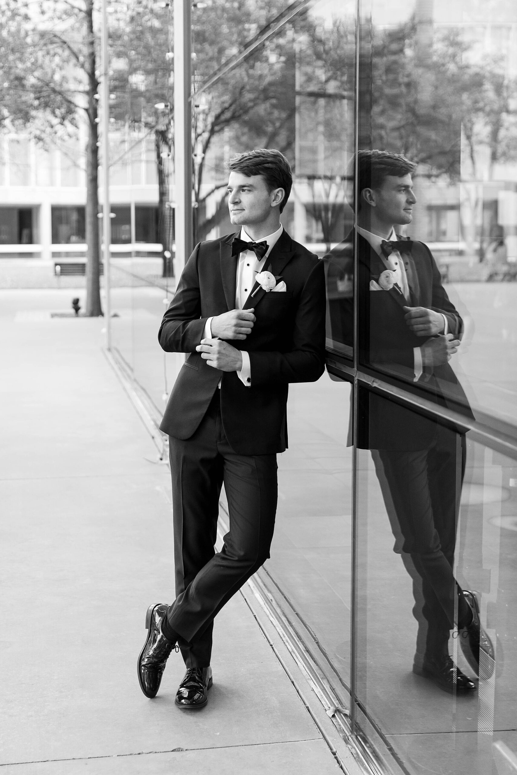 groom leans against glass windows of the Statler Hotel