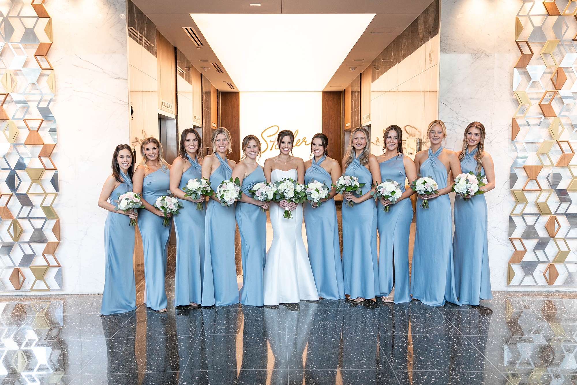 bride and bridesmaids in light blue gowns hold white bouquets inside the lobby at the Statler Hotel