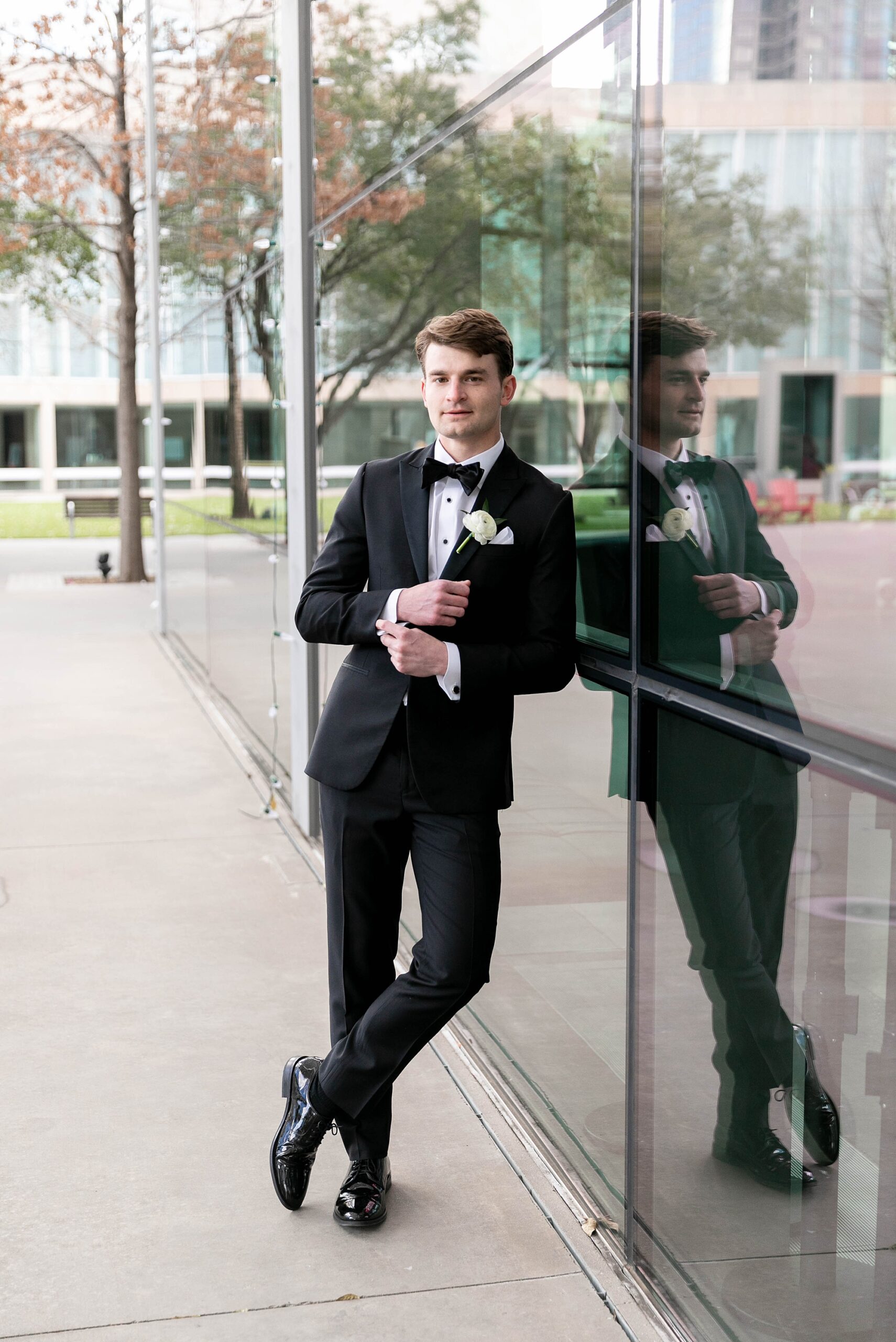 groom leans against glass wall at the Hotel Statler