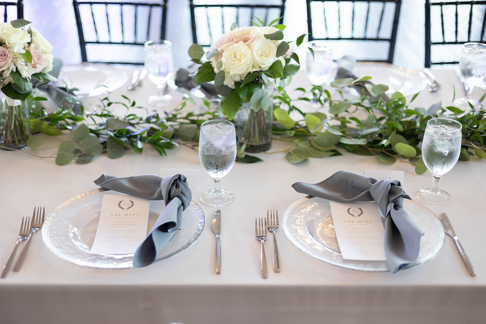 sweetheart table with blue napkins, white and pink flowers, and greenery for wedding reception at the Room on Main