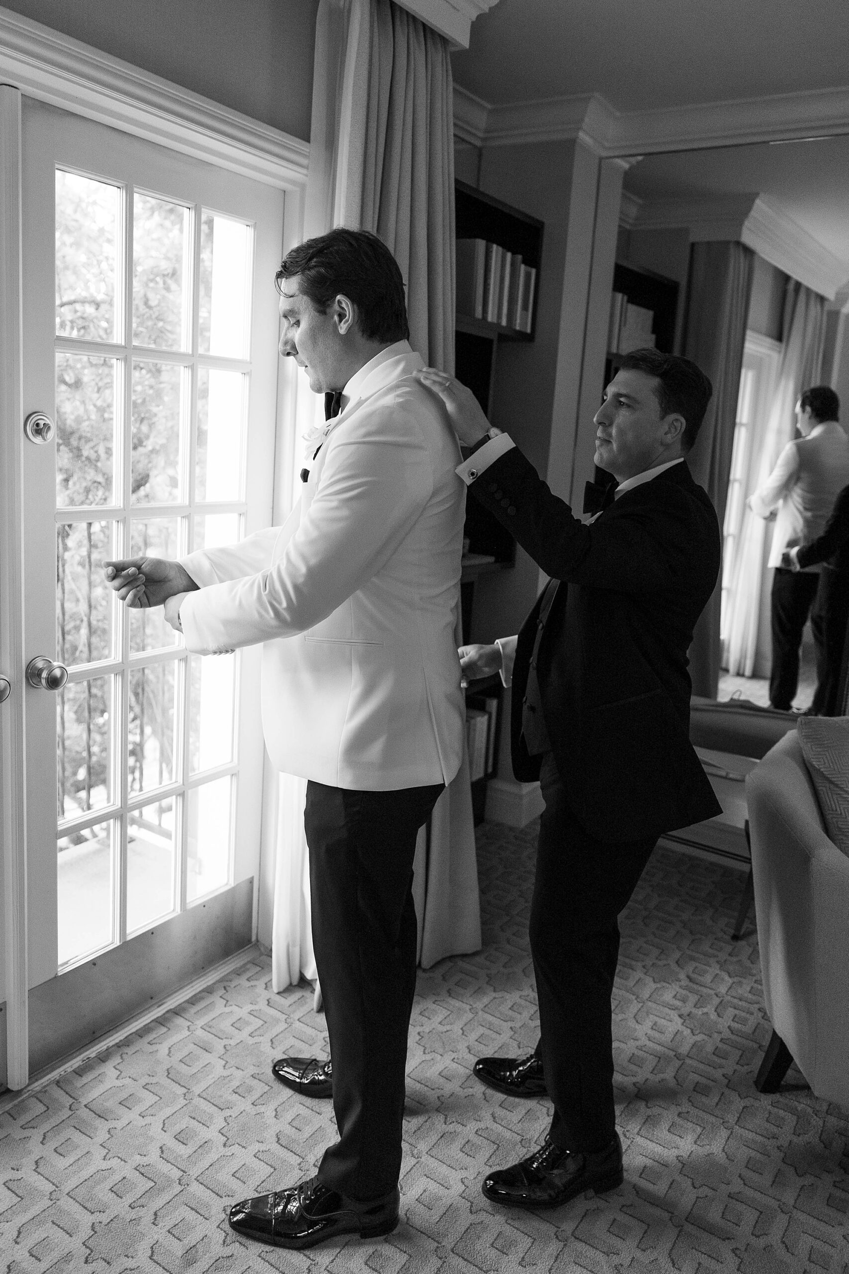 groomsman helps groom into white tux jacket at Rosewood Mansion